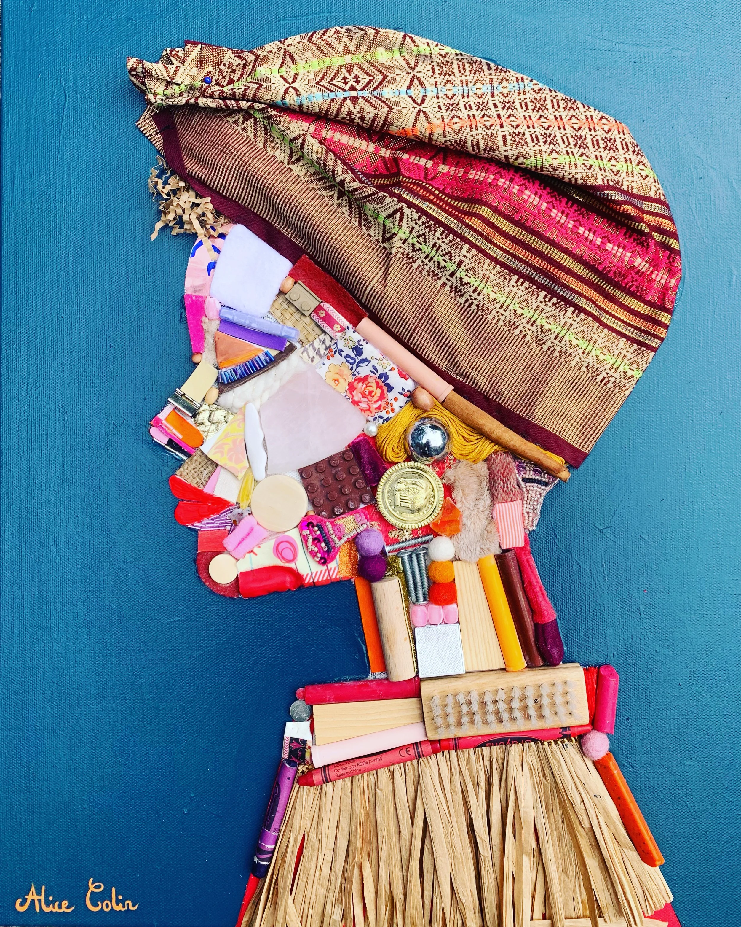 A craft project resembling a hula dancer made from various small objects and materials on a blue background. The head is made from a patterned fabric, and the body is constructed from glittery, floral, and textured materials, with wooden sticks for the legs. The signature 'Alice Colin' is visible in the bottom left corner.