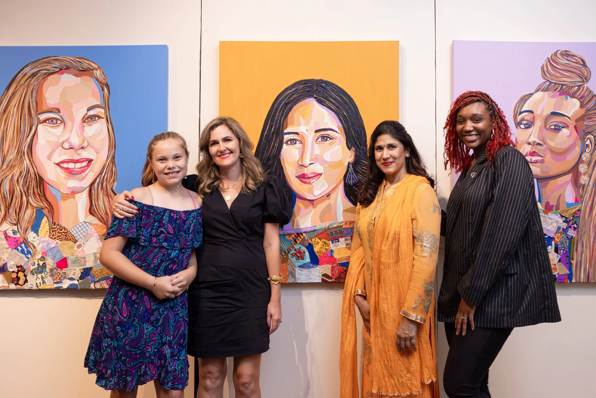 Five women standing in front of colorful portrait paintings at an art gallery.