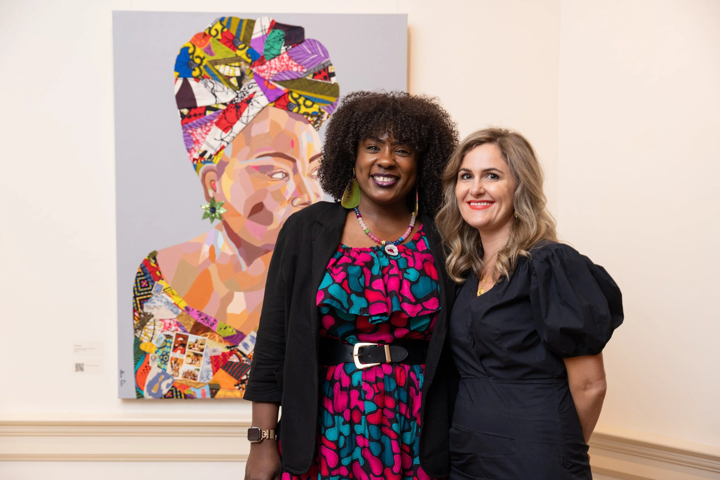 Two women standing in front of a colorful abstract artwork at an art gallery, smiling at the camera.