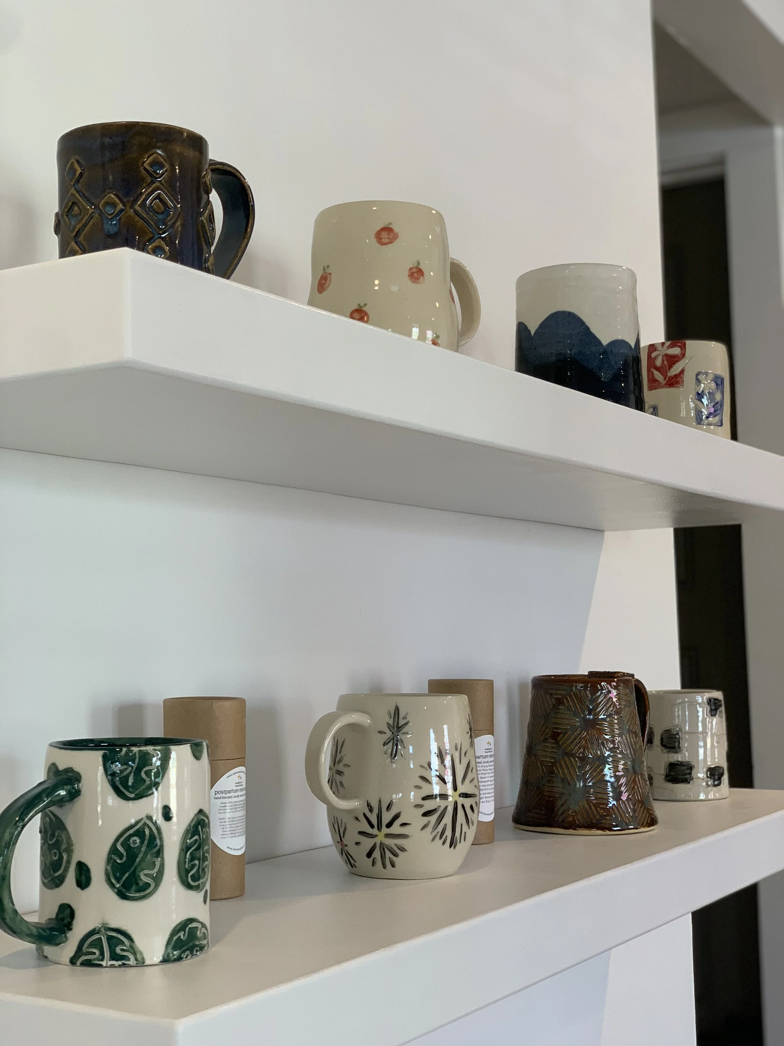 Display shelves with various ceramic mugs and cups, some with artistic patterns and others with natural textures.