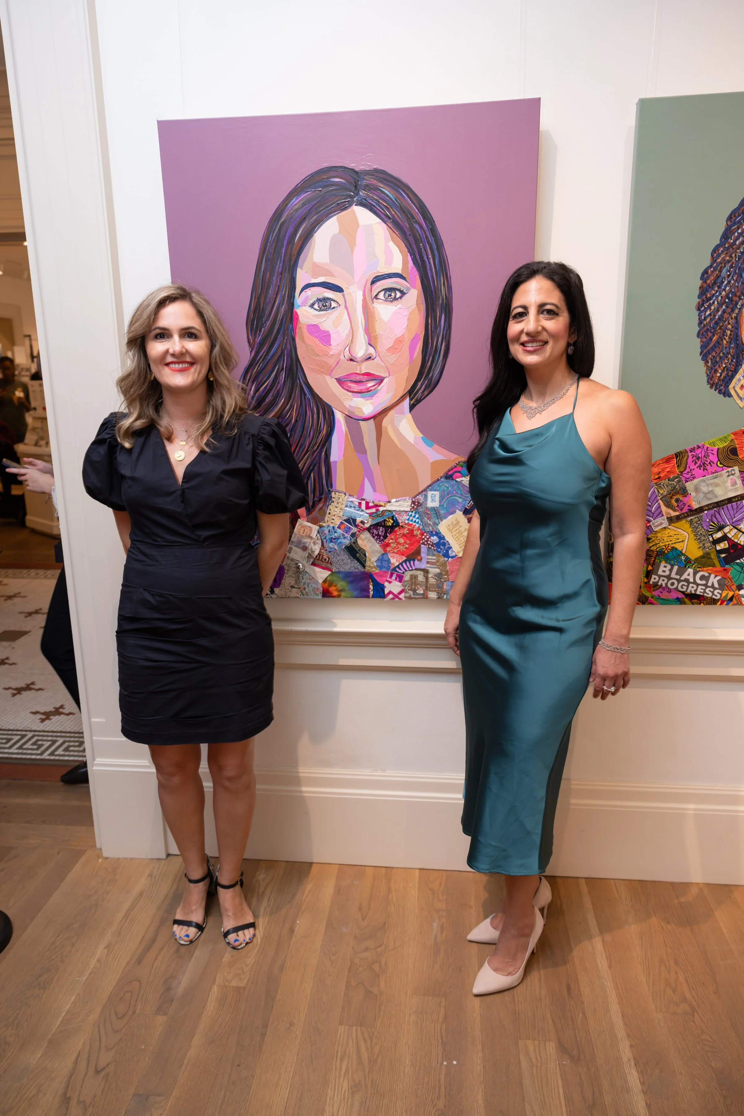 Two women in formal dresses standing in front of an abstract portrait painting at an art gallery event.