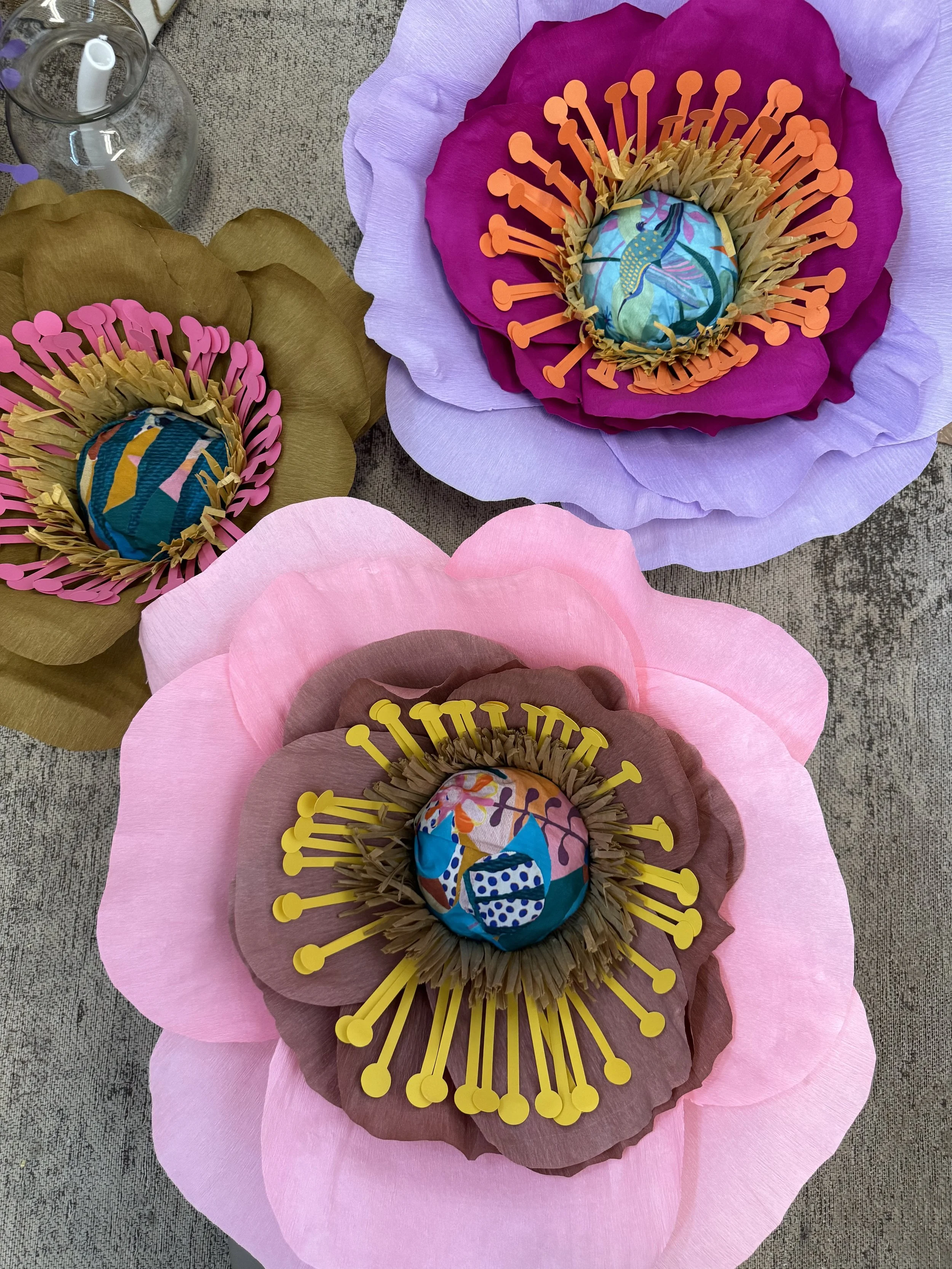 Colorful paper flowers with fabric-covered eggs in the center, placed on a textured surface.