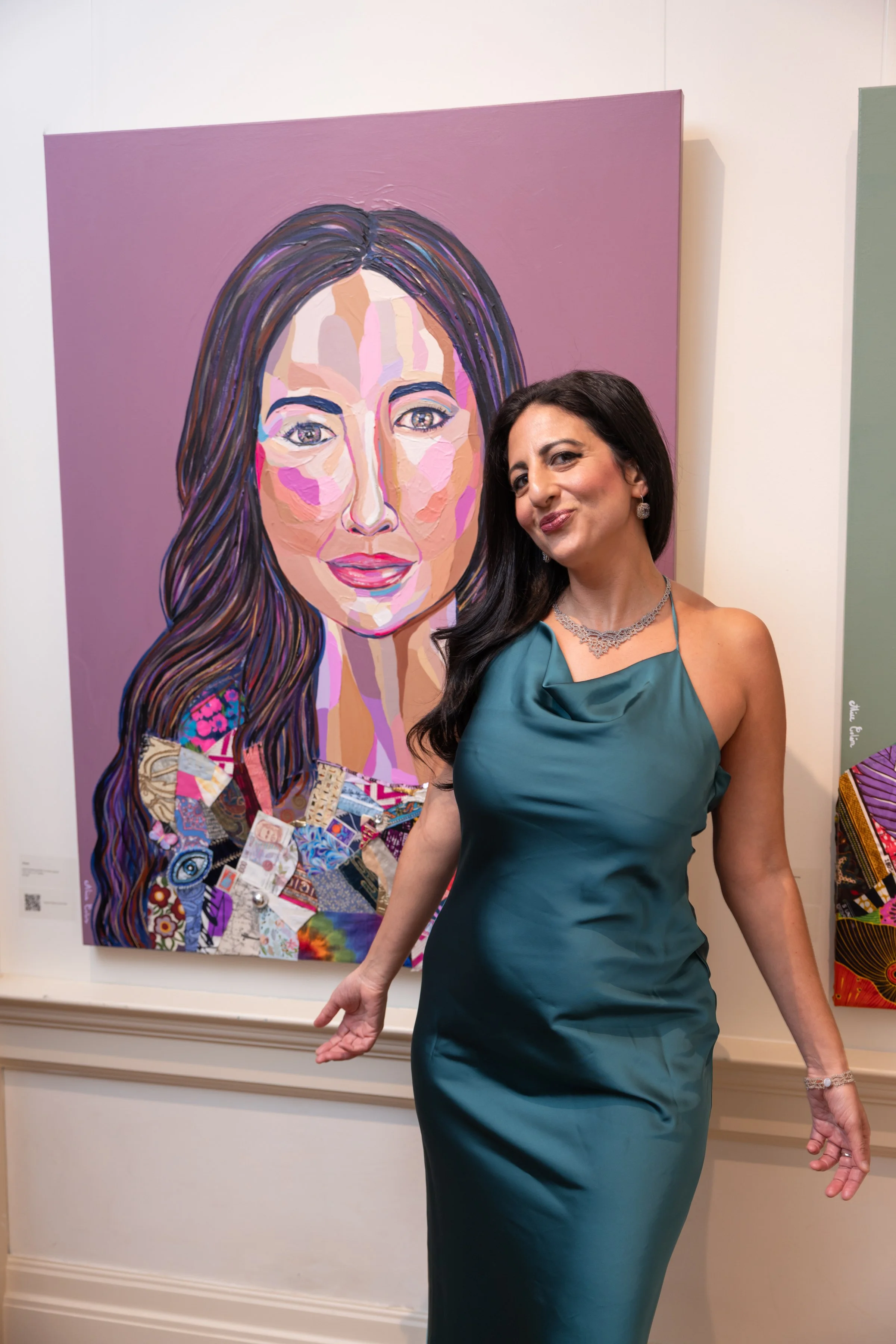 A woman in a teal satin dress standing next to a colorful portrait painting of a woman with long hair, wearing earrings and makeup, at an art gallery.