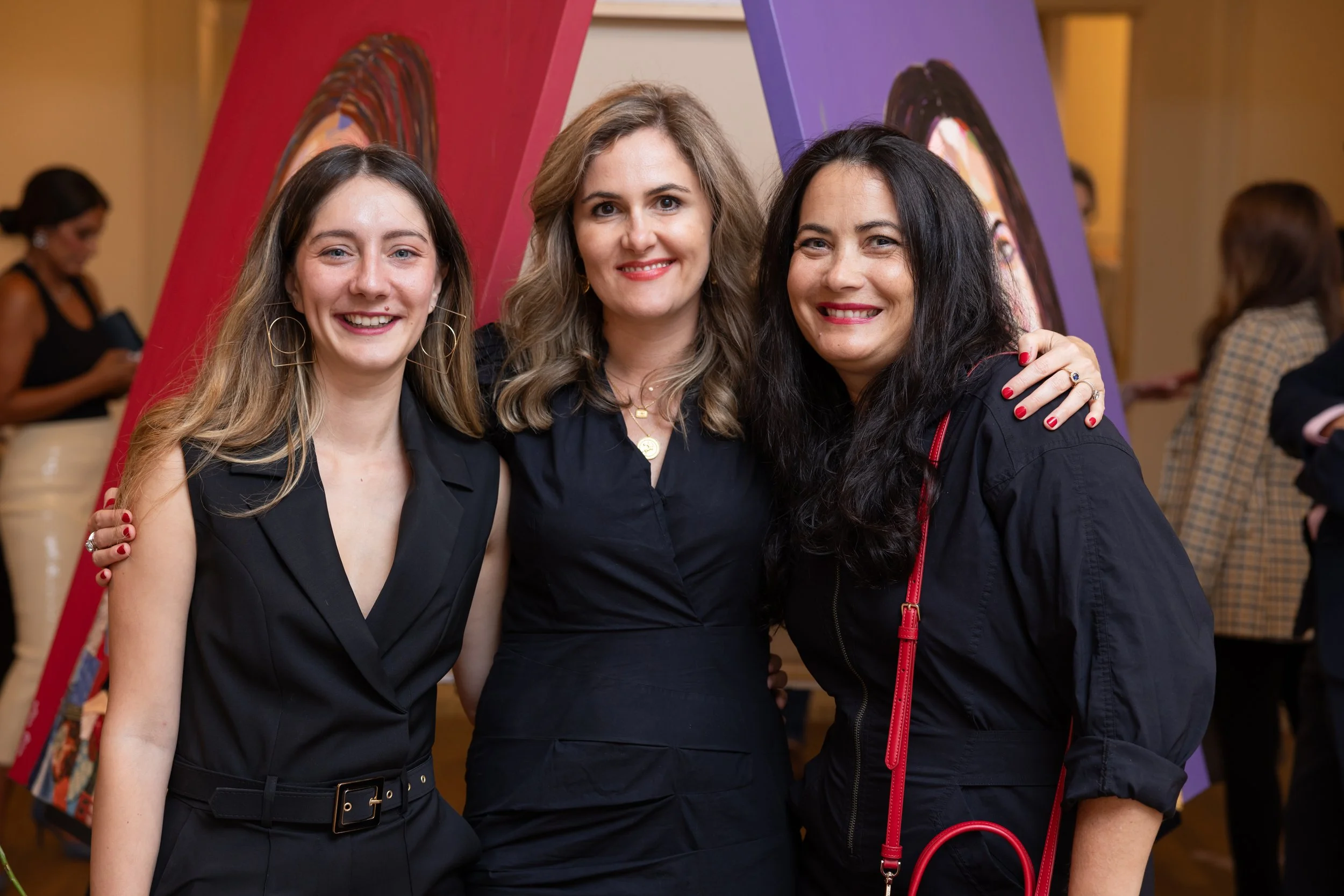 Three women smiling and posing together at an indoor event.