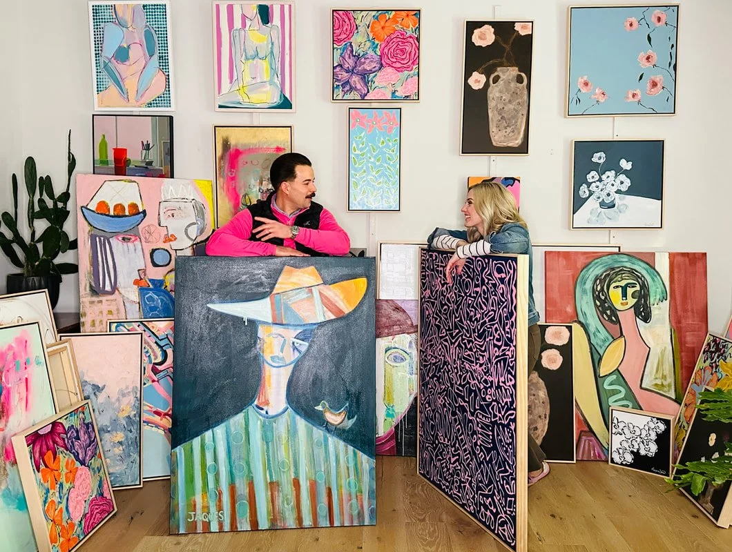 Two people talking in an art gallery surrounded by colorful paintings on the walls and floor.
