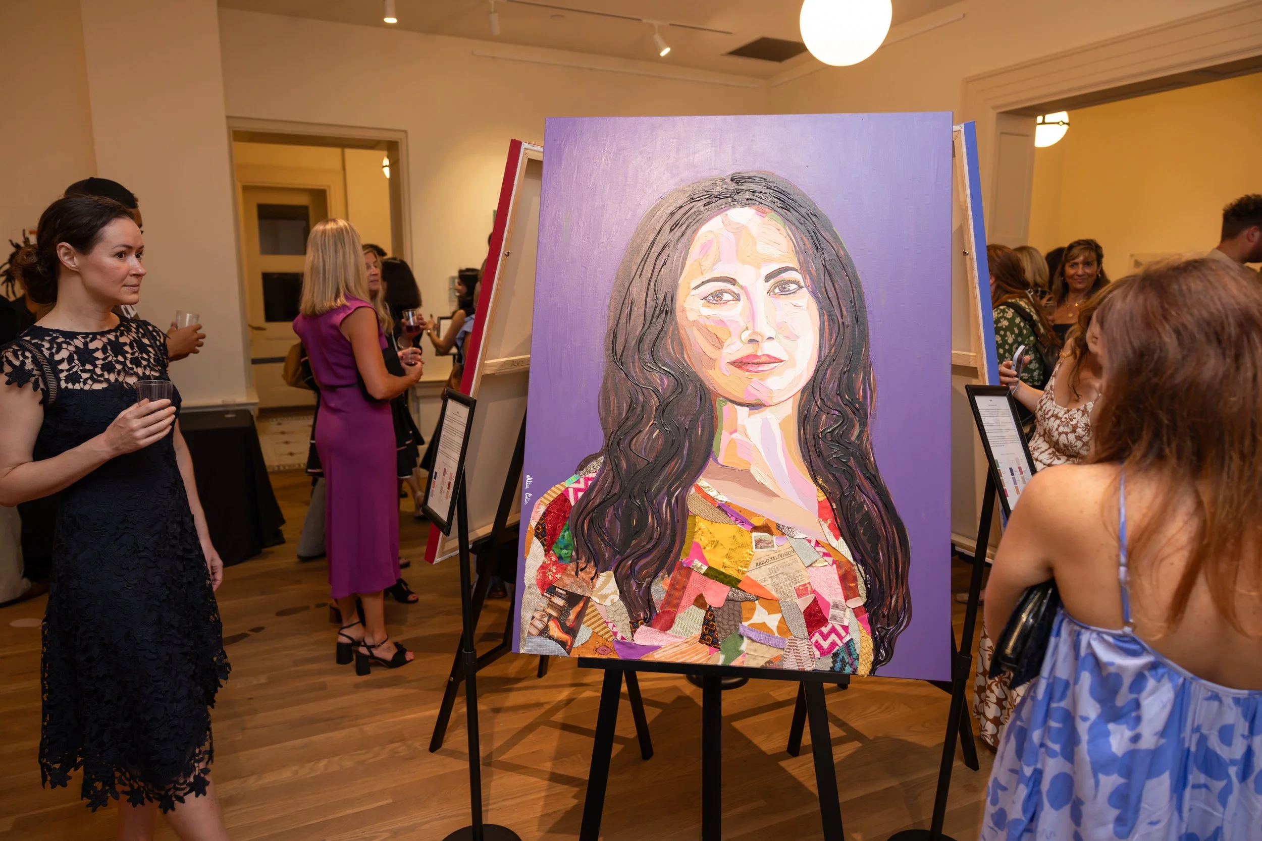 People attending an art exhibit with a large portrait of a woman with long dark hair, composed of colorful collage and painted elements, displayed on an easel in a well-lit gallery.