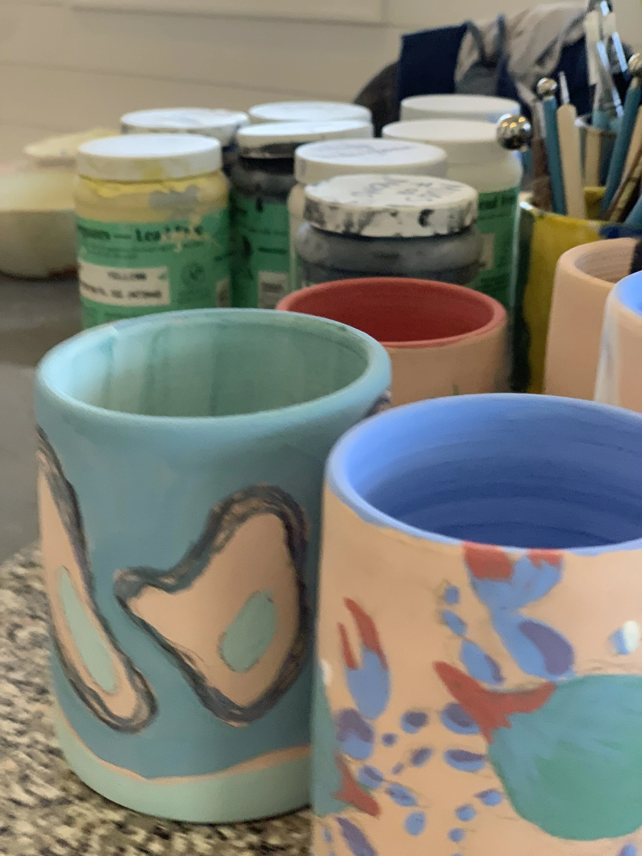 Colorful hand-painted ceramic cups with abstract designs on a shelf.