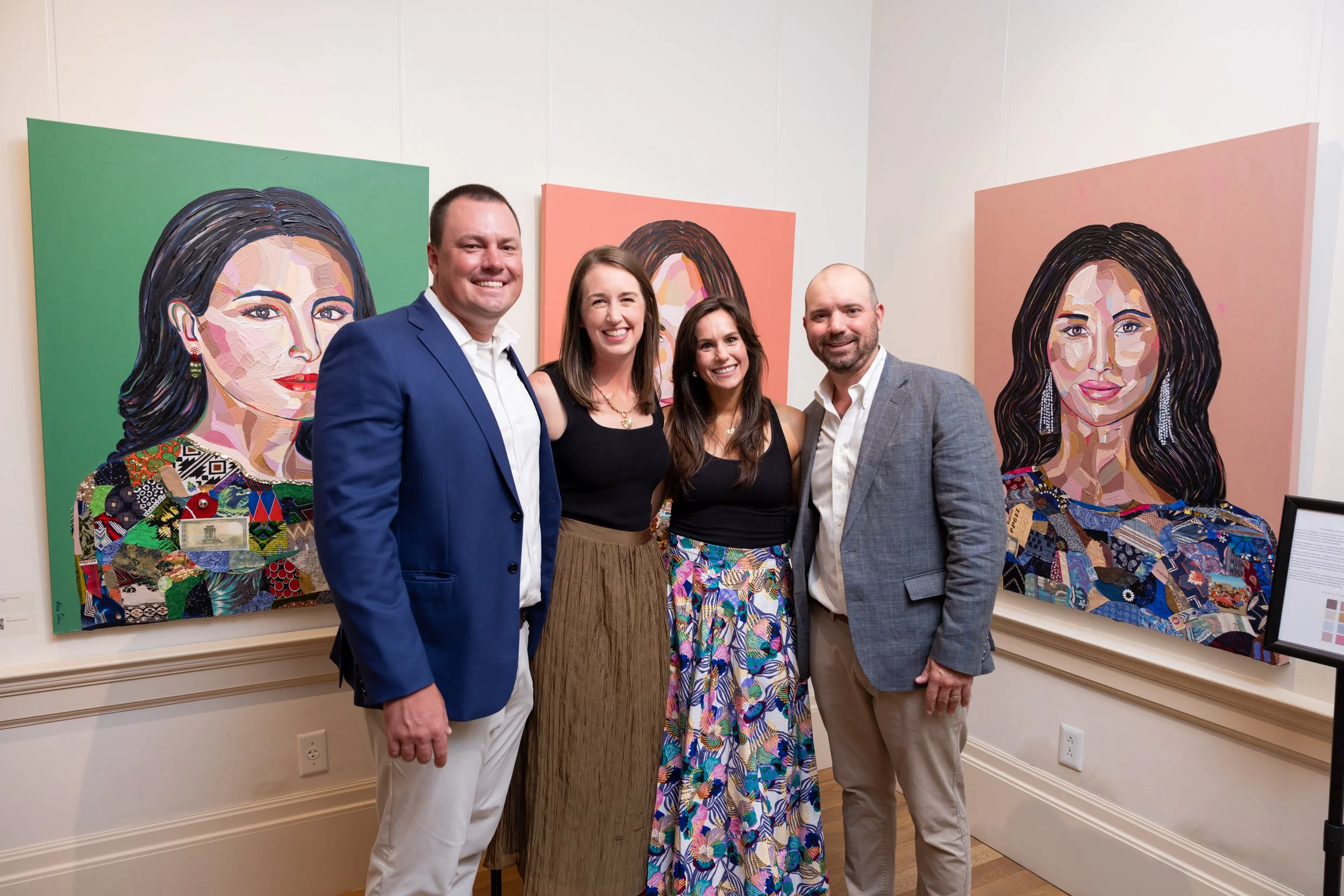 A group of five people standing in front of colorful portrait paintings at an art gallery. They are smiling and dressed in semi-formal attire.