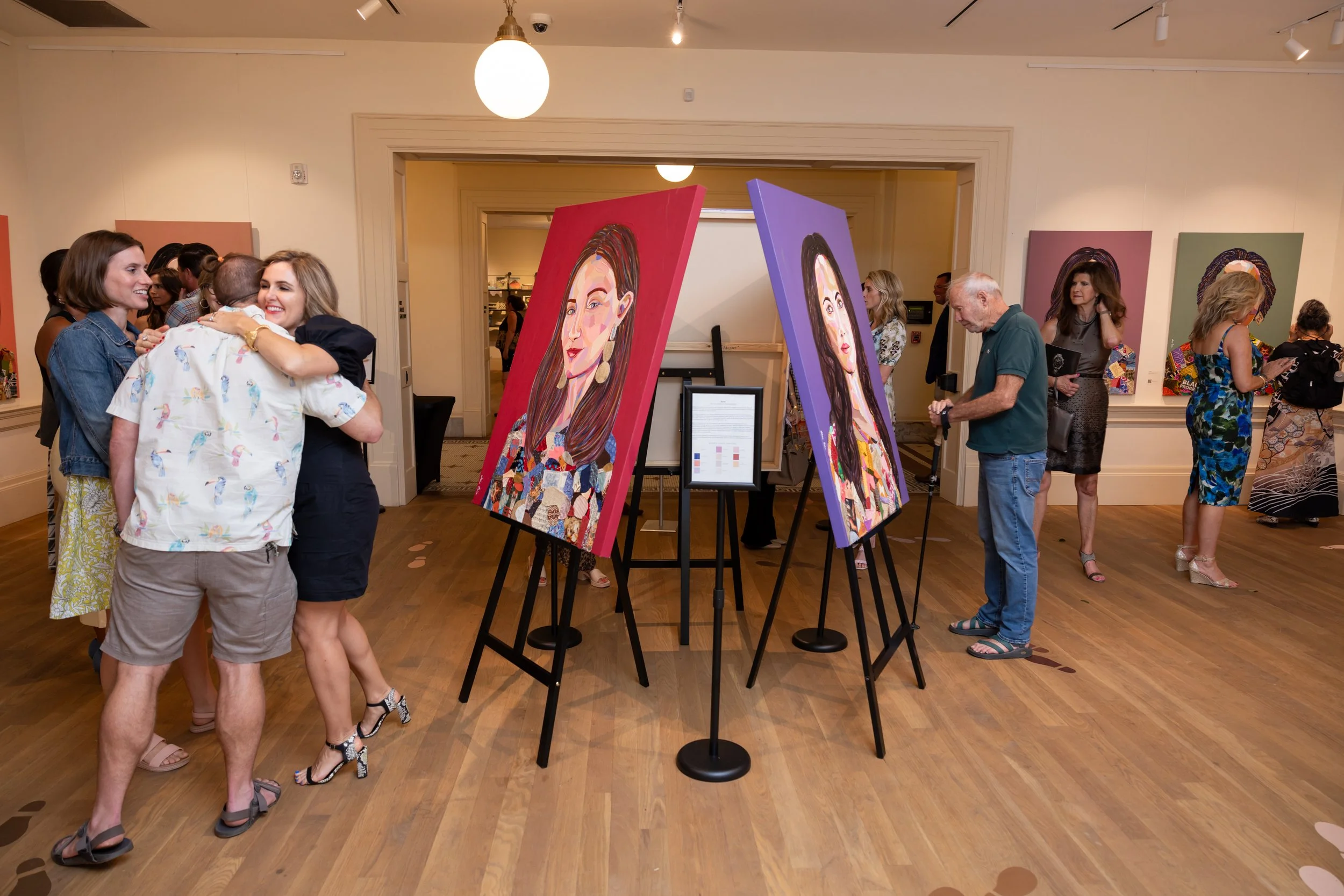 People viewing colorful portrait paintings in an art gallery or exhibition space.