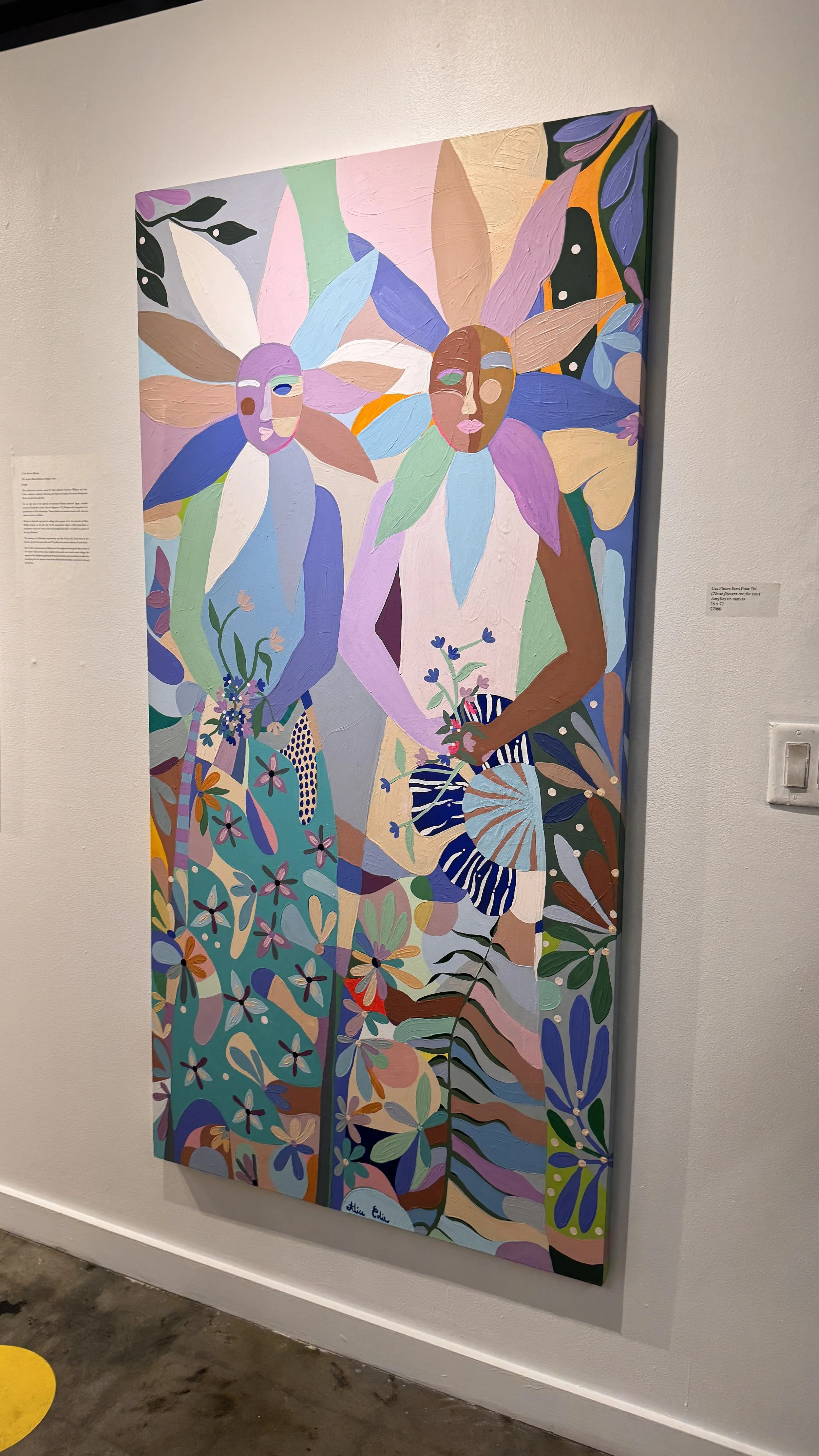 Colorful abstract painting of three women with floral surroundings displayed on a gallery wall.