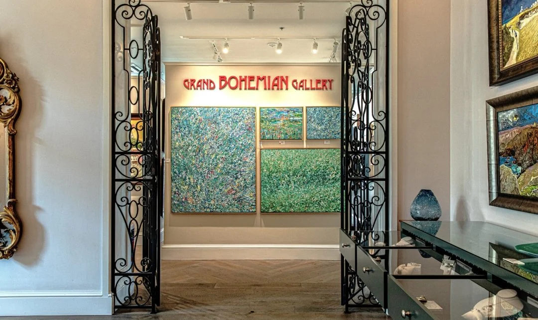 The entrance to the Grand Bohemian Gallery with three colorful abstract paintings and a sign above reading "Grand Bohemian Gallery" in red letters, with decorative black wrought iron gates on either side.