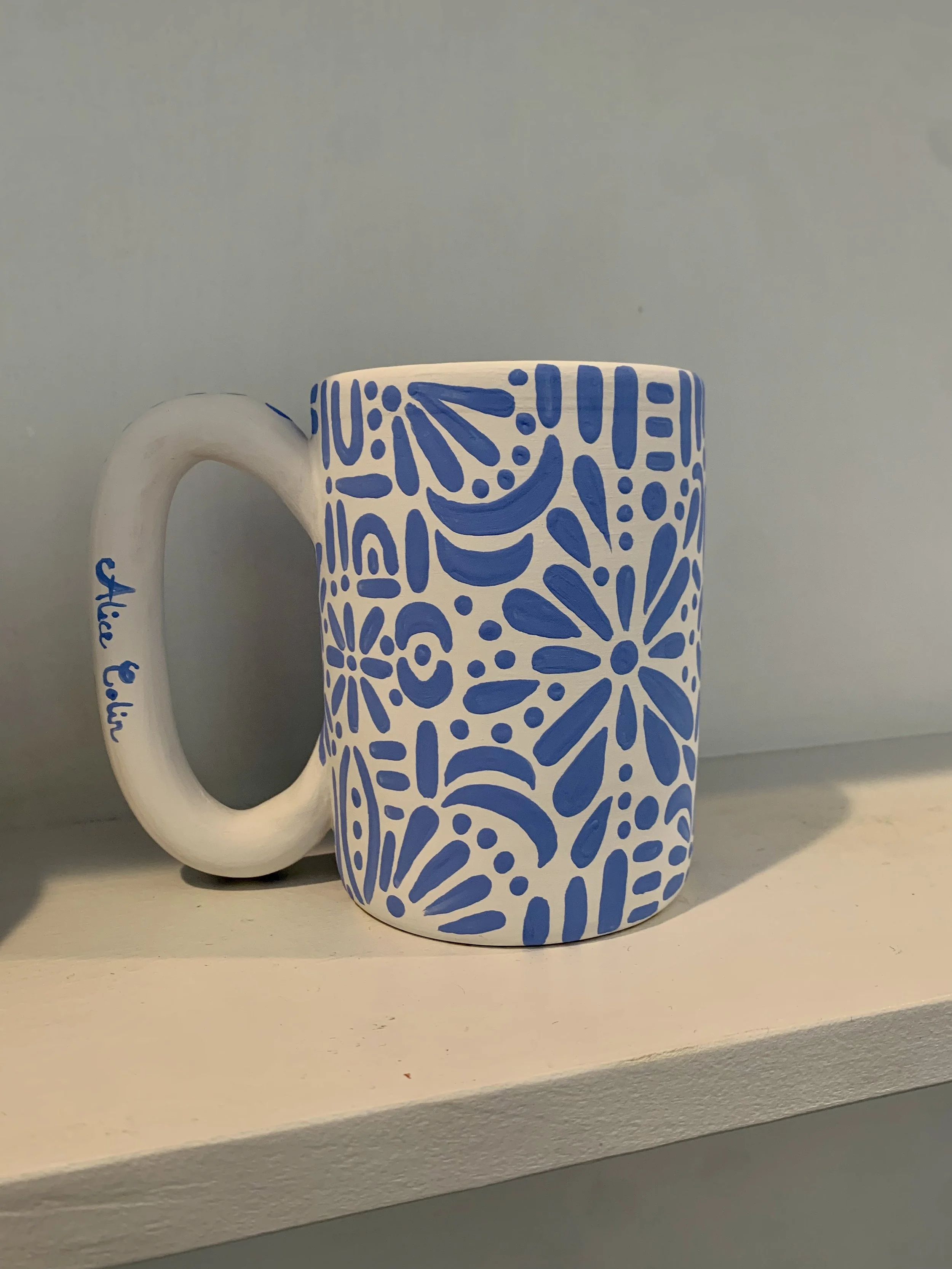 Close-up view of a ceramic mug with a blue floral pattern on a white background, placed on a white surface.