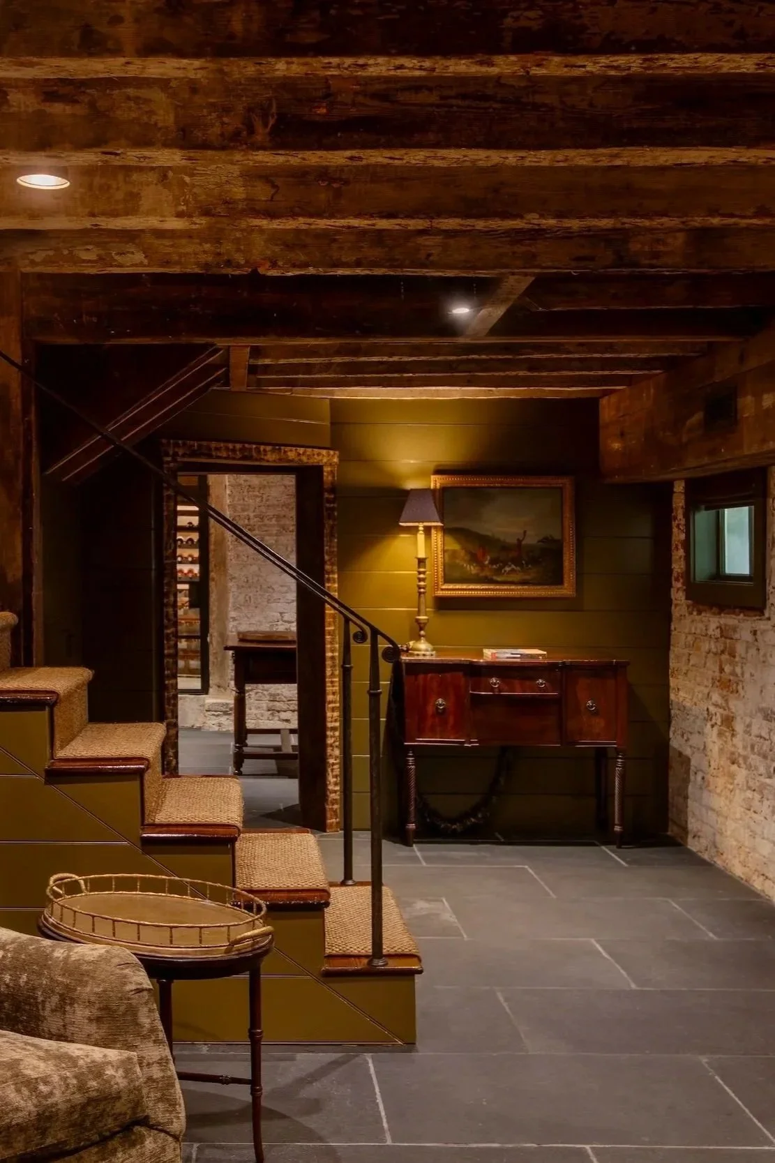 Interior view of a basement or under-croft with wood-beam ceilings and an exposed brick wall.