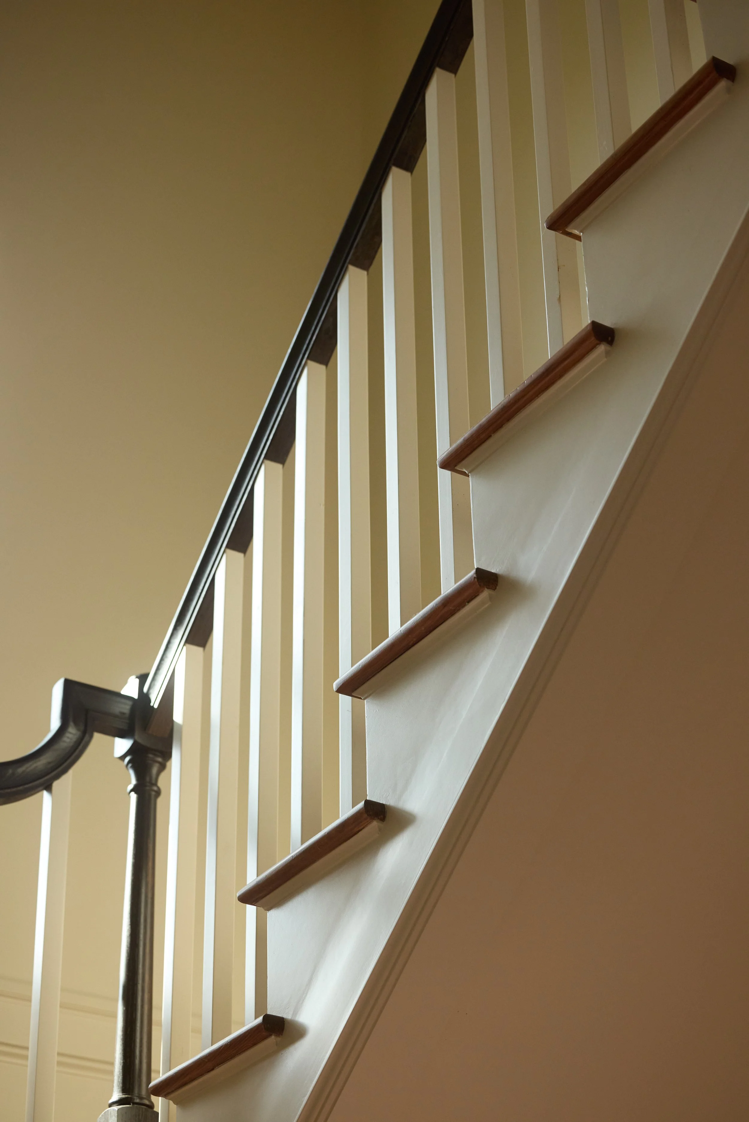 Interior view of a staircase with wooden steps, a dark handrail, and white balusters, viewed from below.