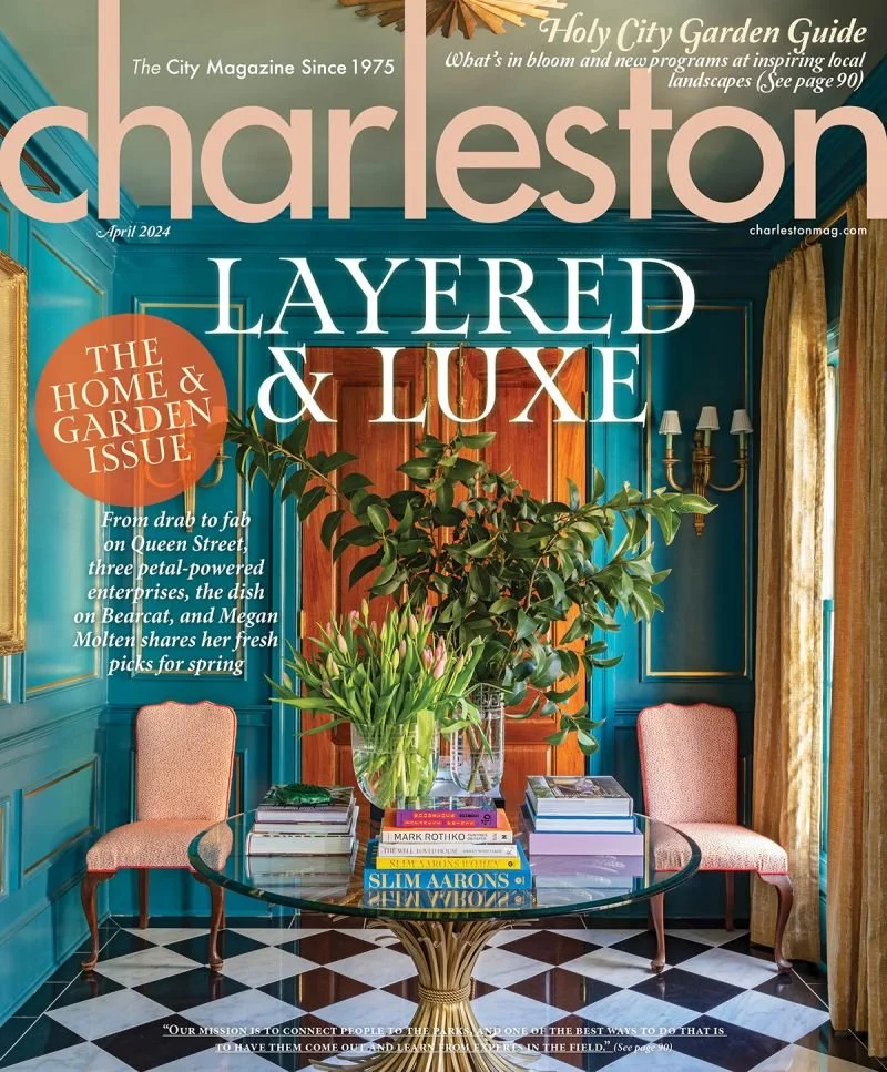 Magazine cover titled 'Charleston' featuring a teal-colored room with two pink upholstered chairs, a glass table with books and a large vase of pink tulips and green foliage, a wooden door, gold curtains, a blue wall with gold wall sconces, and a black-and-white checkered floor.