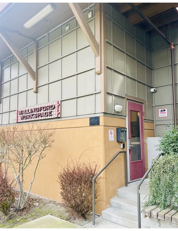 Exterior of a building with a sign that reads 'Waltersford Workspace,' a maroon door with steps, and bushes in front.