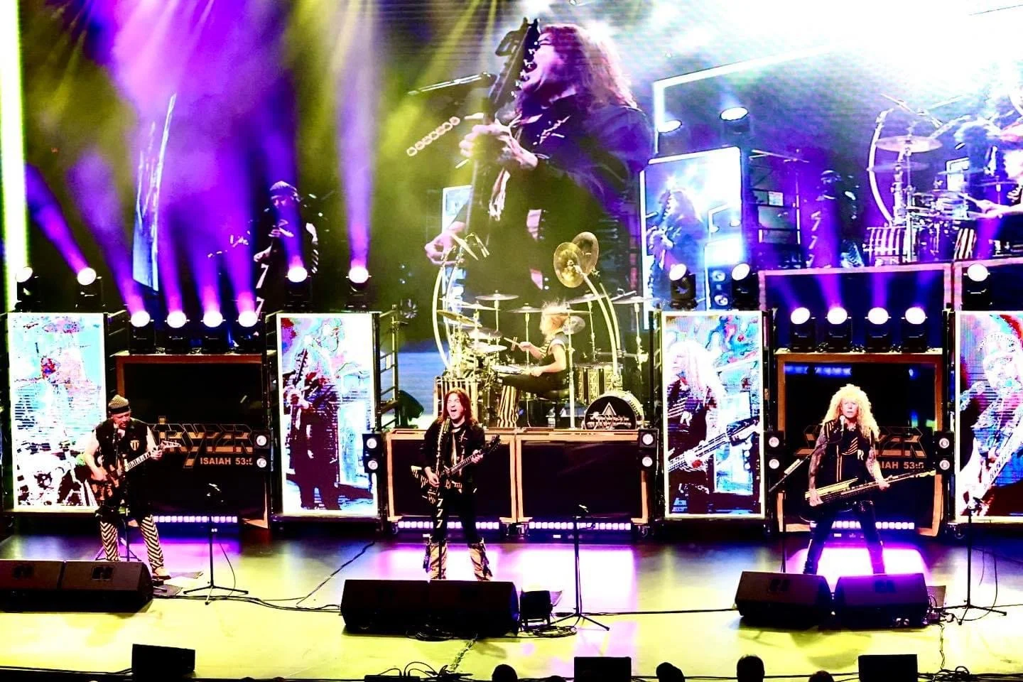 A band performing live on stage with multiple musicians, colorful lights, and large digital screens in the background.