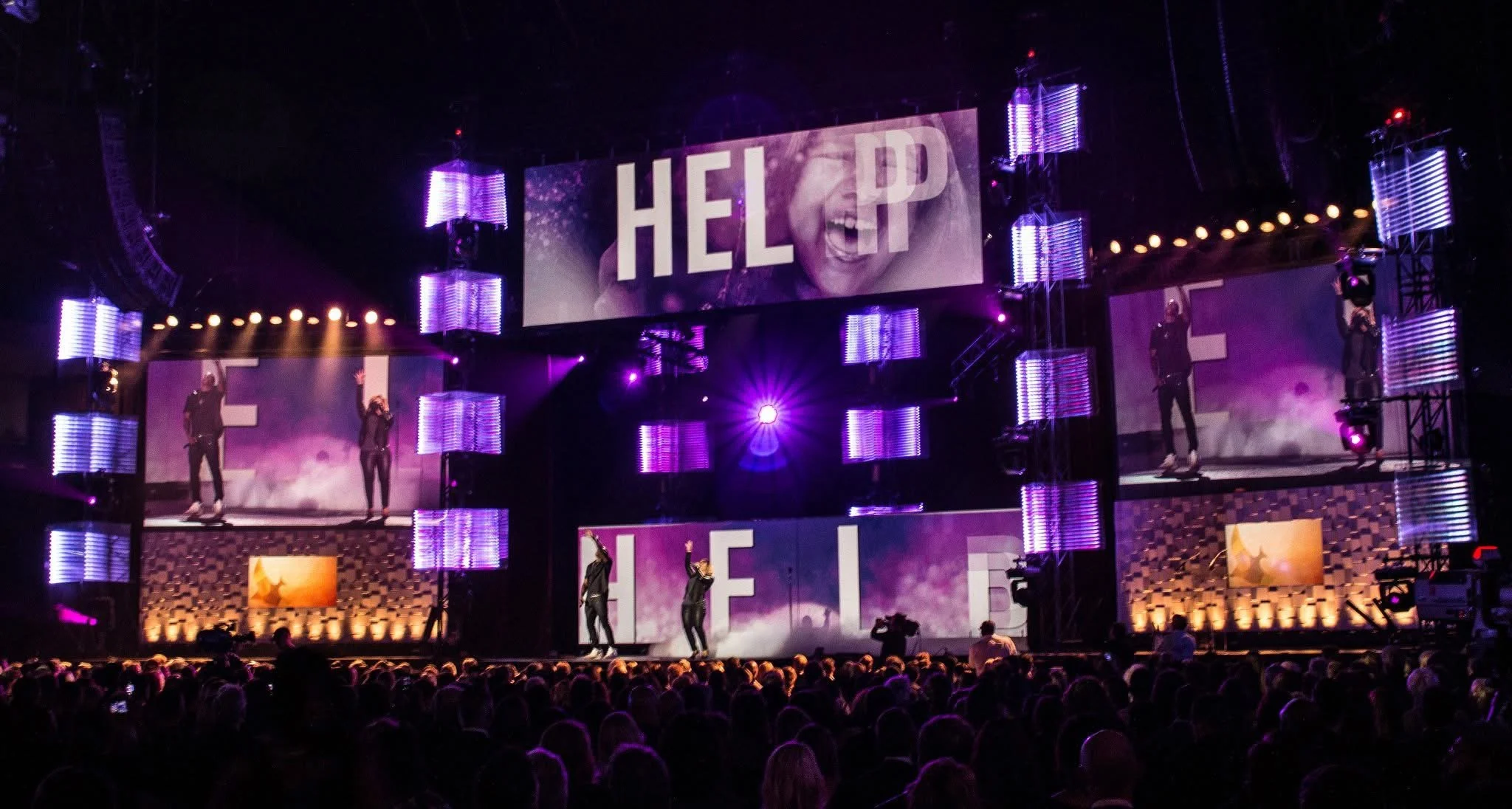 A stage with performers and large screens displaying the word 'HELP' at a concert or event.
