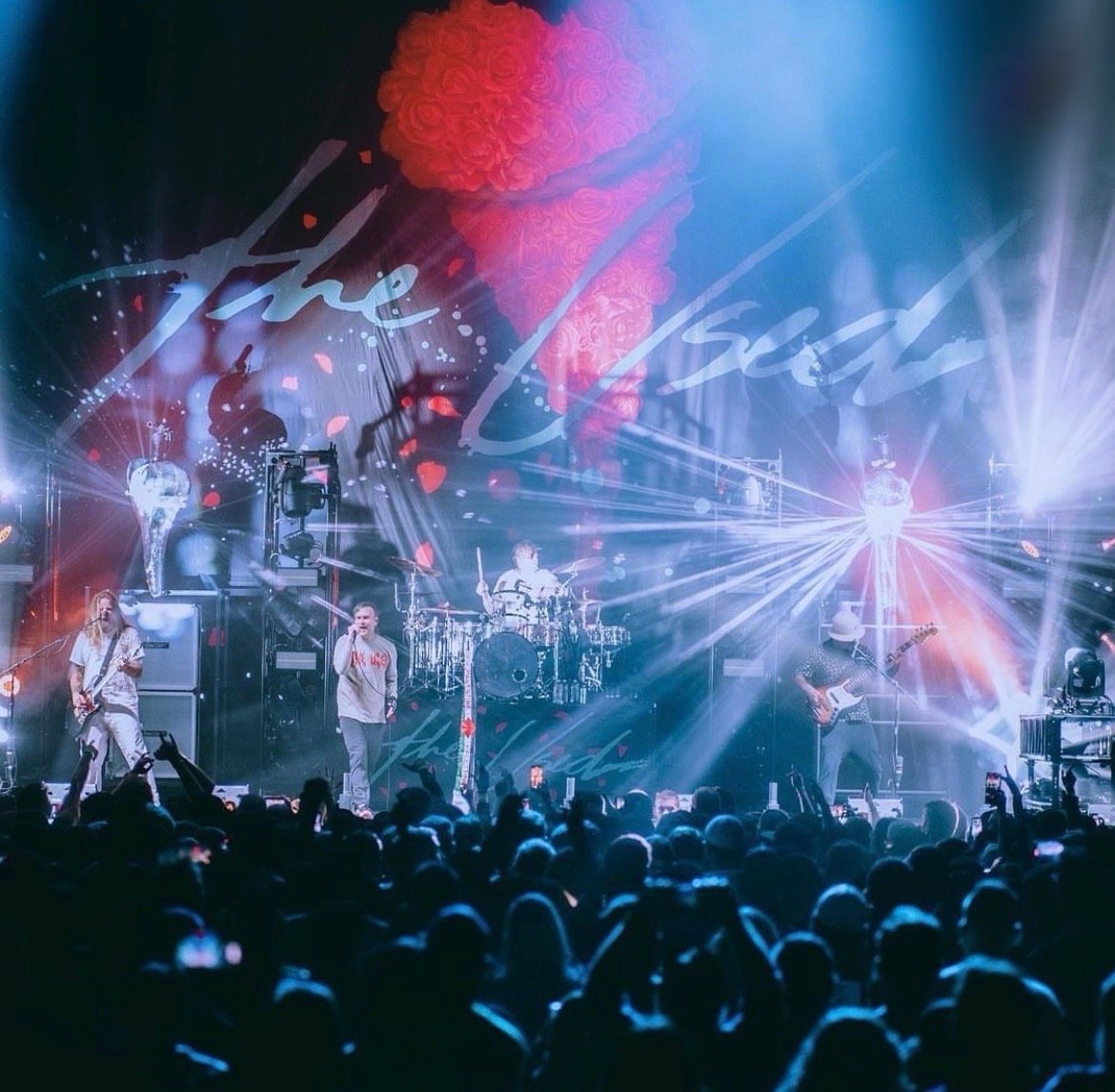 A live concert with a band performing on stage, bright lighting effects, and a large audience watching.