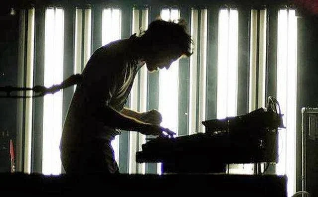 Person operating a DJ or music equipment in front of illuminated curtains.