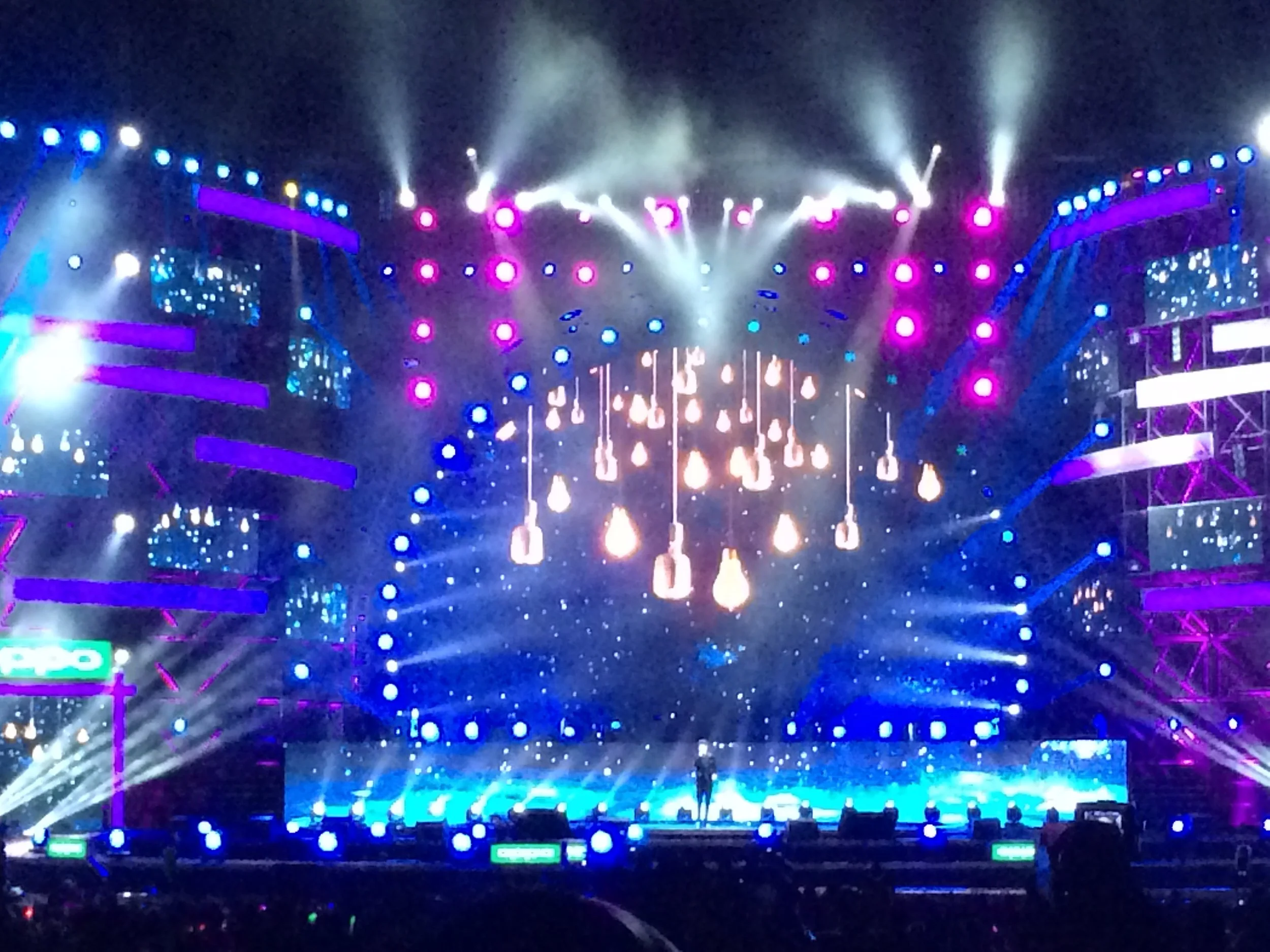 A stage with bright purple, blue, and white lights creating a vibrant atmosphere, showing an audience watching a performance or event.