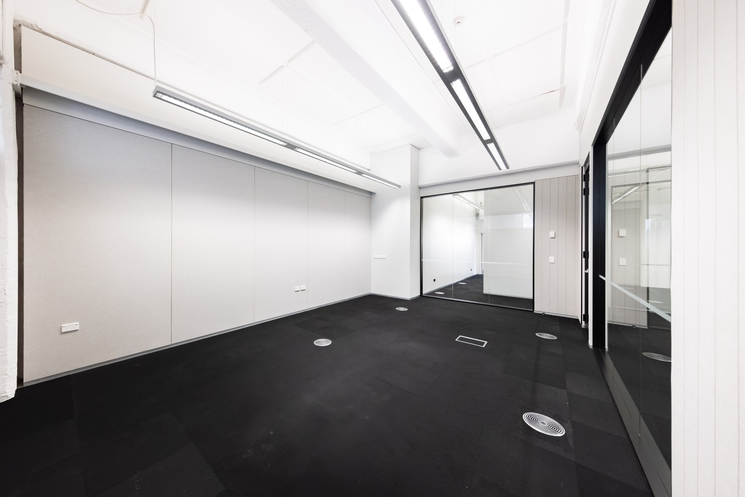 Te Hau Pūkerikeri - an empty office space at Toi Aro. 33 m² with a capacity of up to 6 people. White walls, dark grey carpet, office with partition walls, glass windows and door.