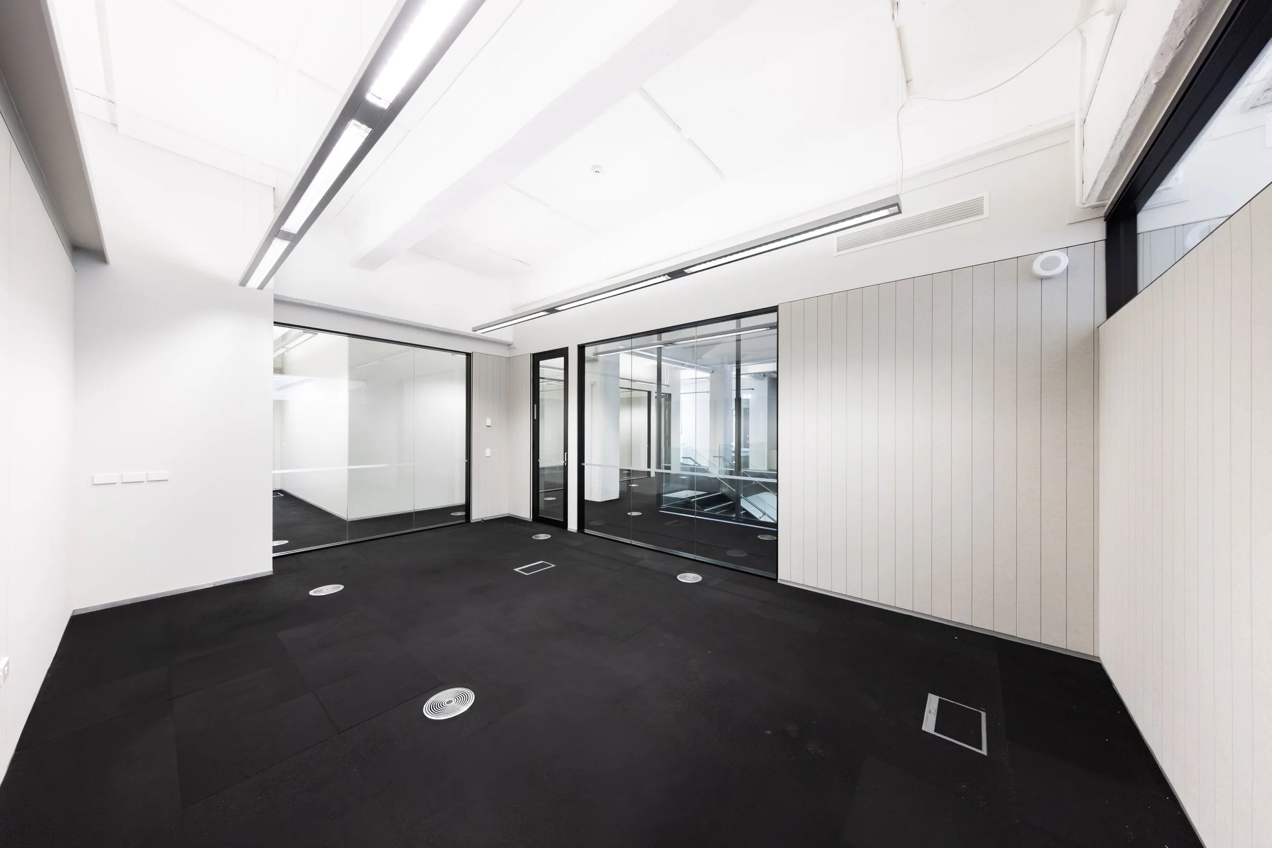 Te Hau Pūkerikeri - an empty office space at Toi Aro. 33 m² with a capacity of up to 6 people. White walls, dark grey carpet, office with partition walls, glass windows and door.