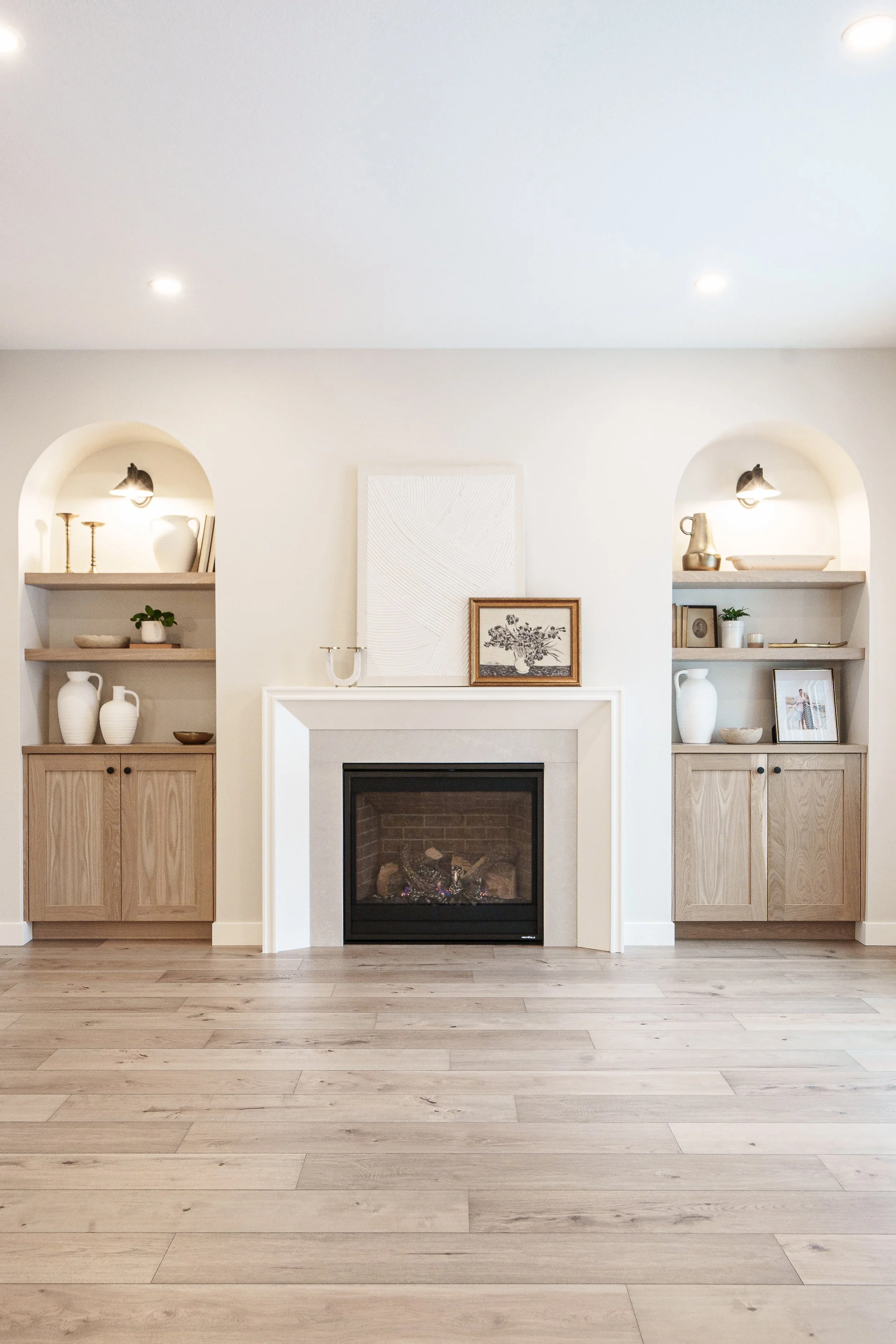 Living room with white walls, a fireplace, built-in wood shelves on either side, and light wood flooring.
