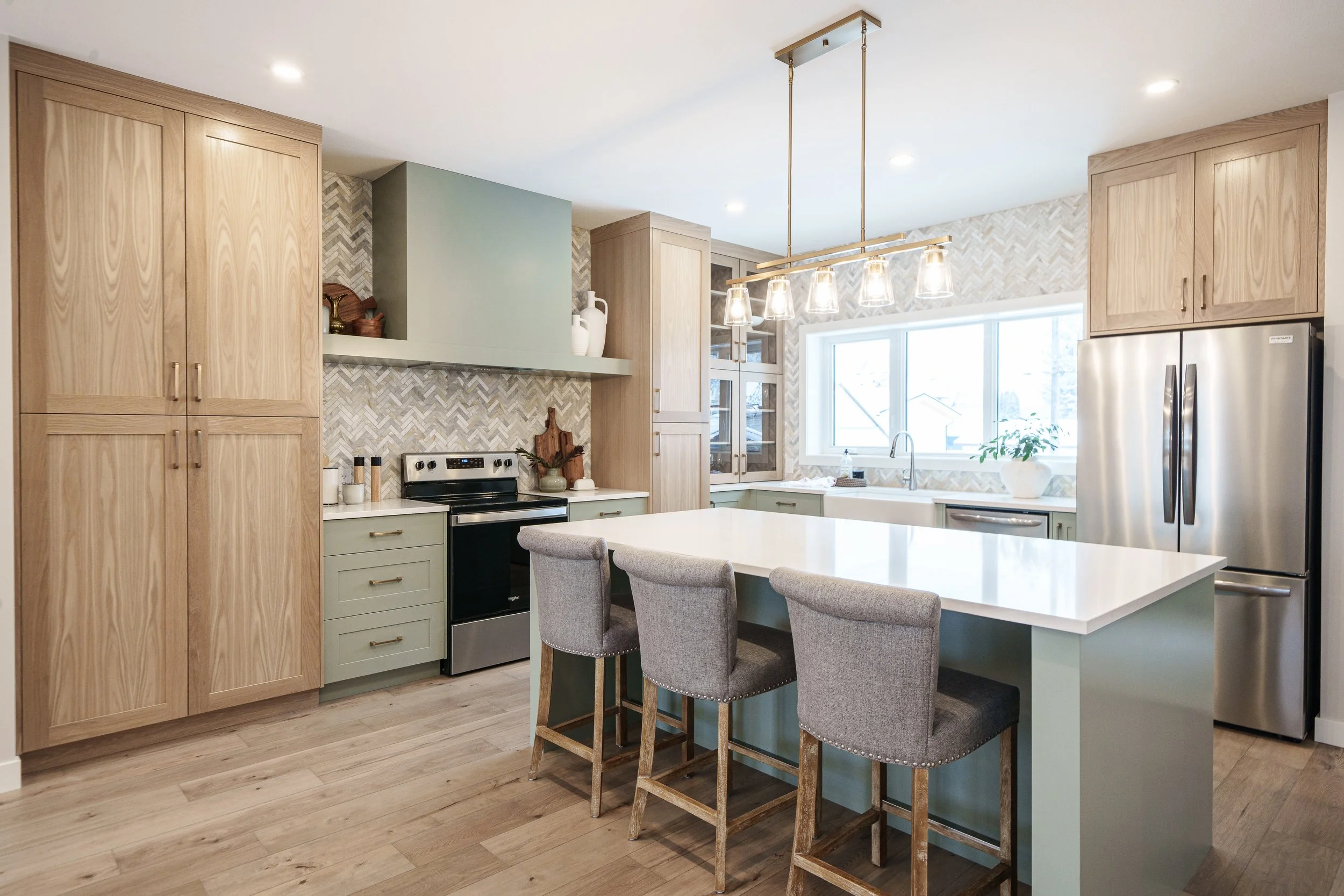 Modern kitchen with wooden cabinets, white countertops, stainless steel appliances, a kitchen island with four gray upholstered bar stools, a large window, and light wood flooring.
