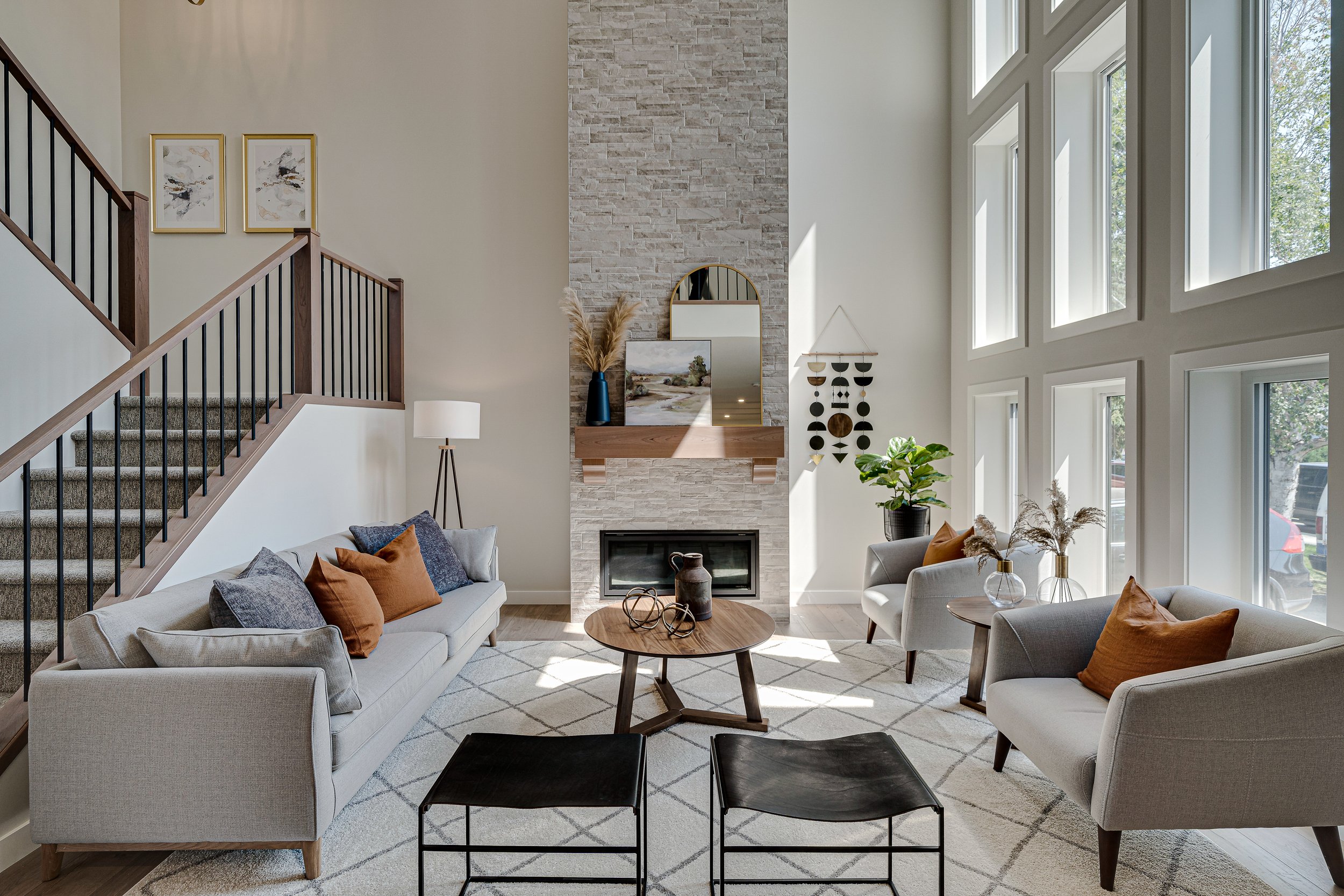 Living room with beige sofas and pillows, a round wooden coffee table, a fireplace with a stone wall, decorative items, and large windows letting in natural light.