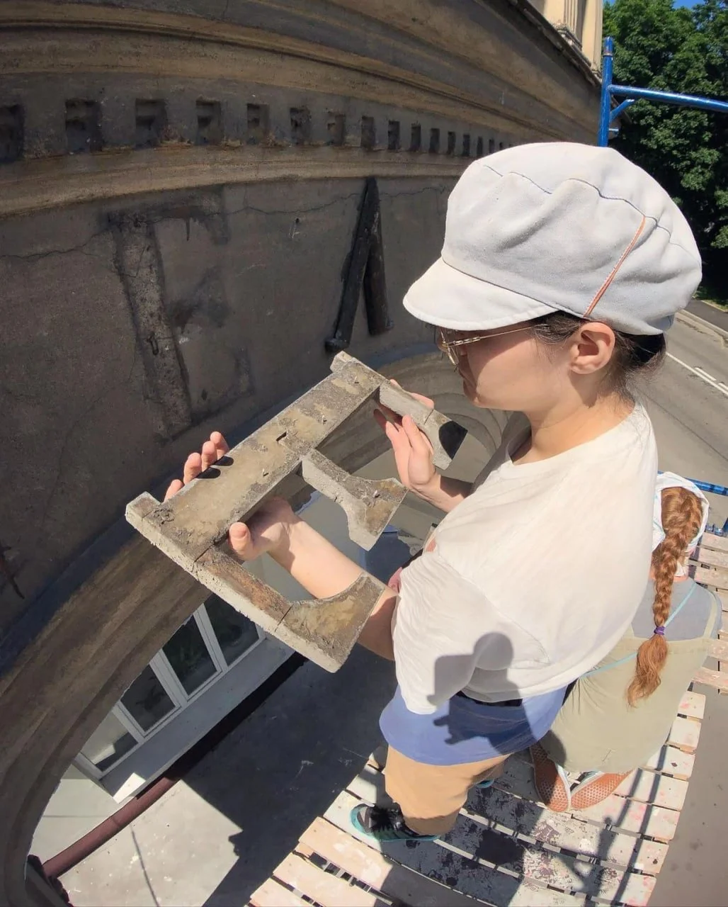 La restauradora Polina Salnikova retira un letrero de madera de la fachada del edificio
Restorer Polina Salnikova is removing a wooden sign from the building's facade