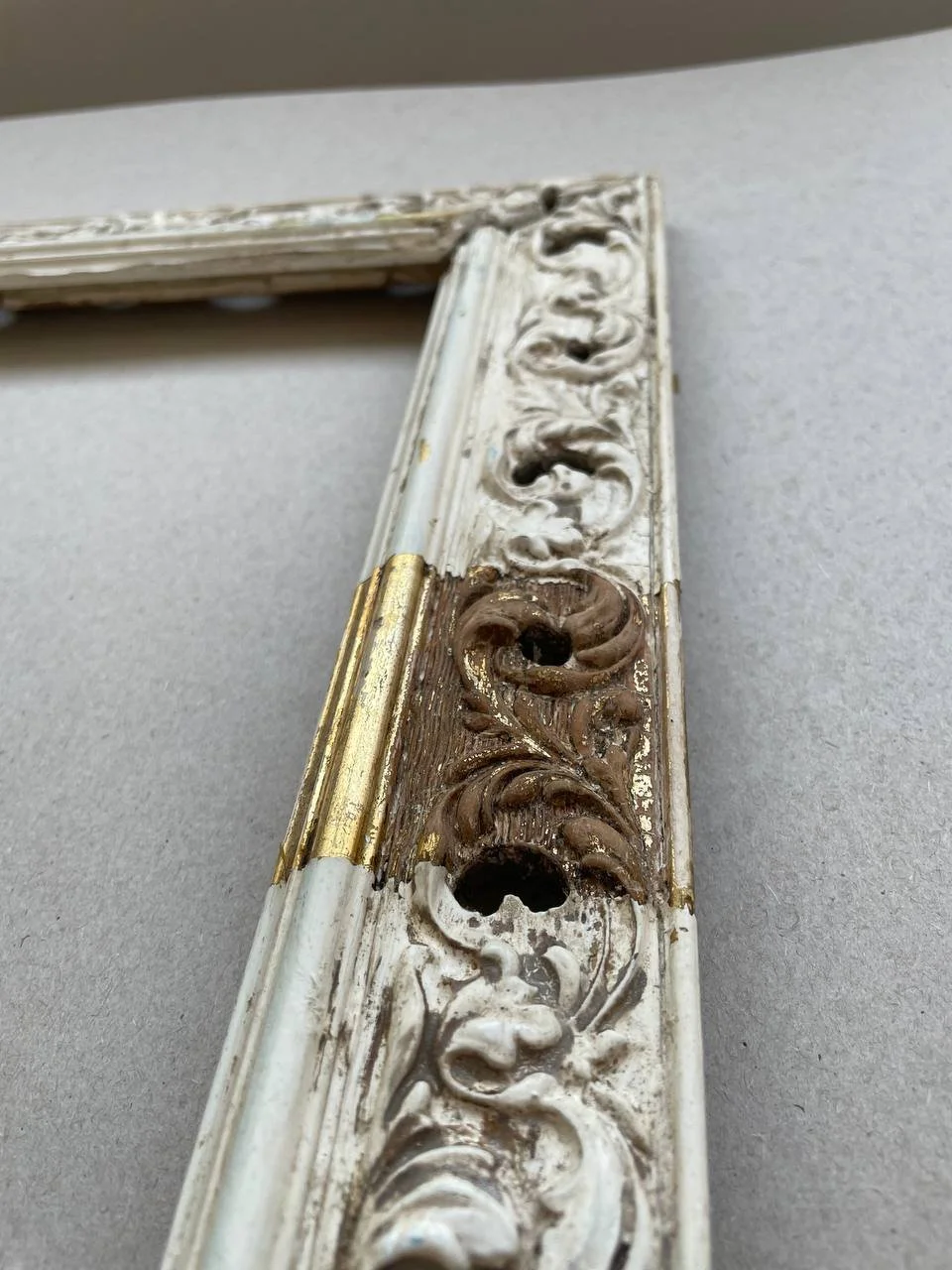Close-up of an antique decorative frame showing signs of damage and wear, with intricate carved patterns in white and gold.