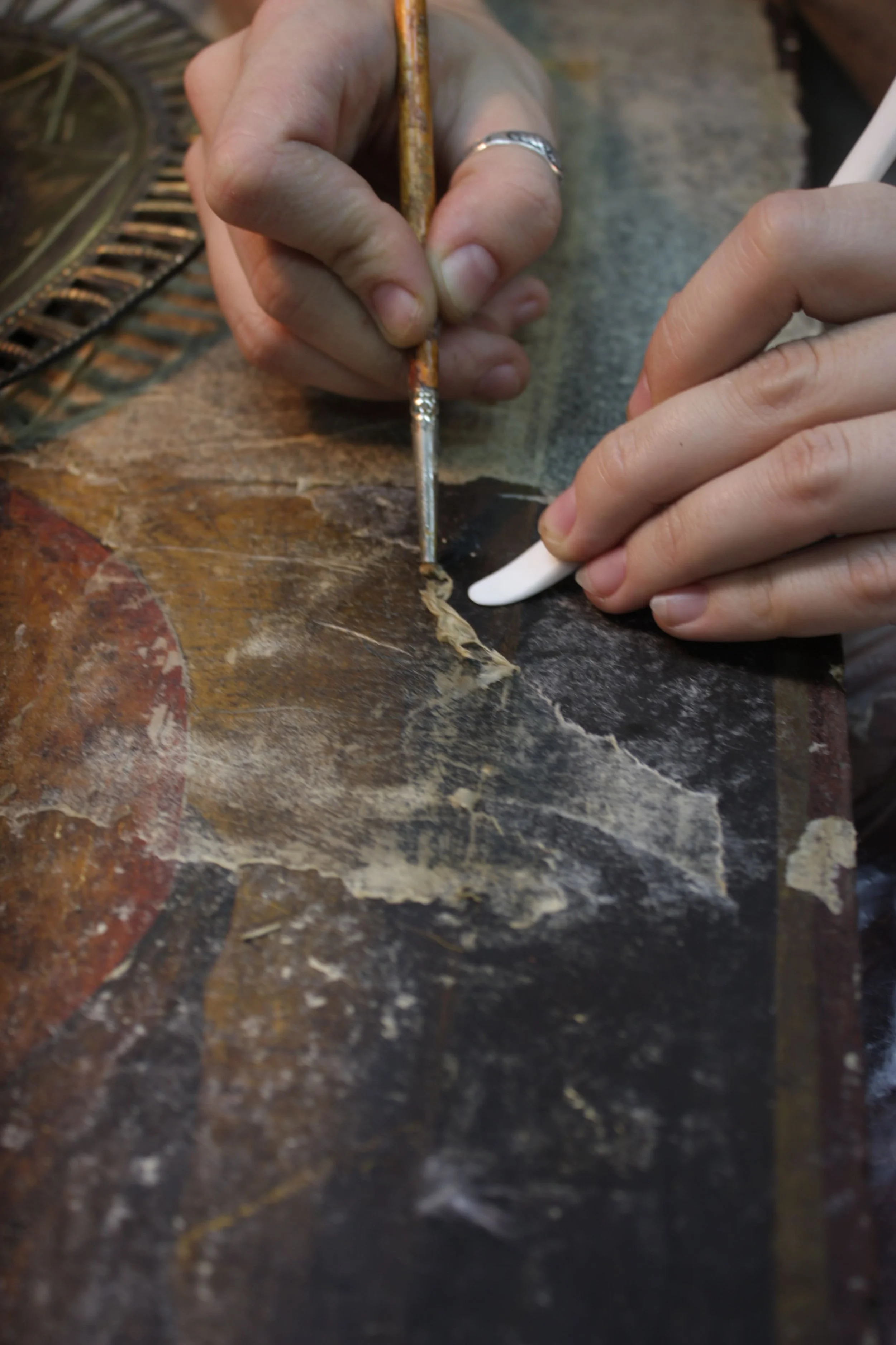 Person restoring a vintage sign with small tools and a brush on a chipped, weathered surface.