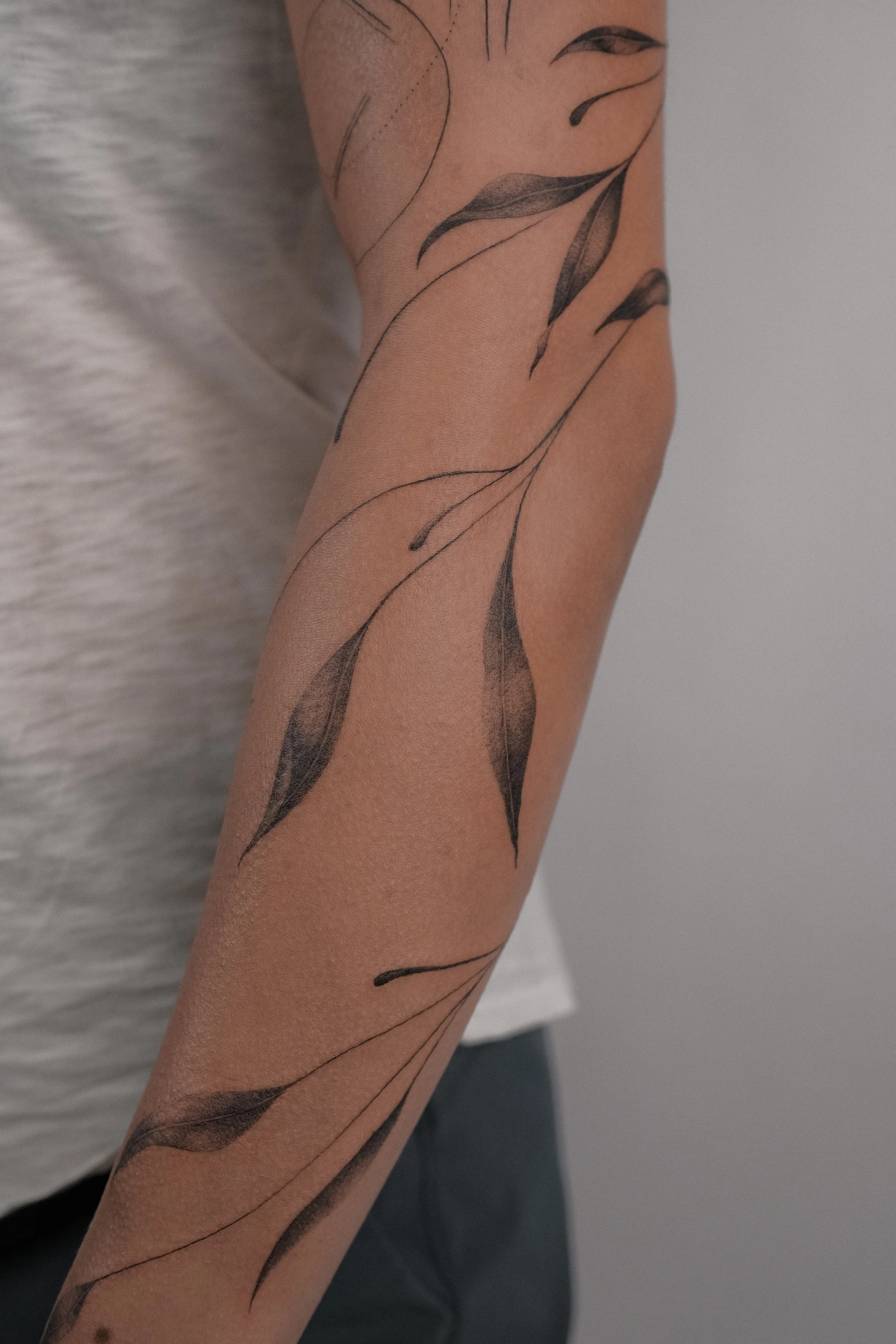 A person's arm with a black ink tattoo of leaves and stems.