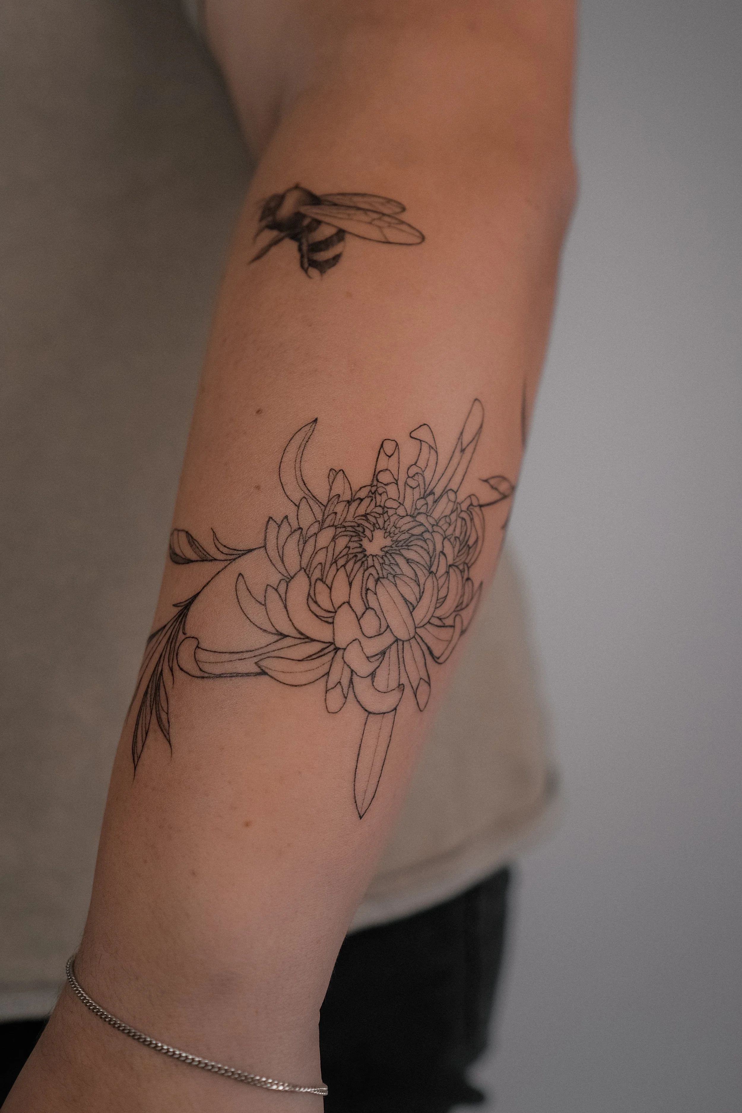 A person's arm with a black outline tattoo of a bee above a large flower tattoo.