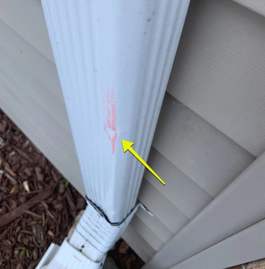 Close-up of a house siding corner showing a vertical white component with a red arrow pointing at a faded red mark or stain.