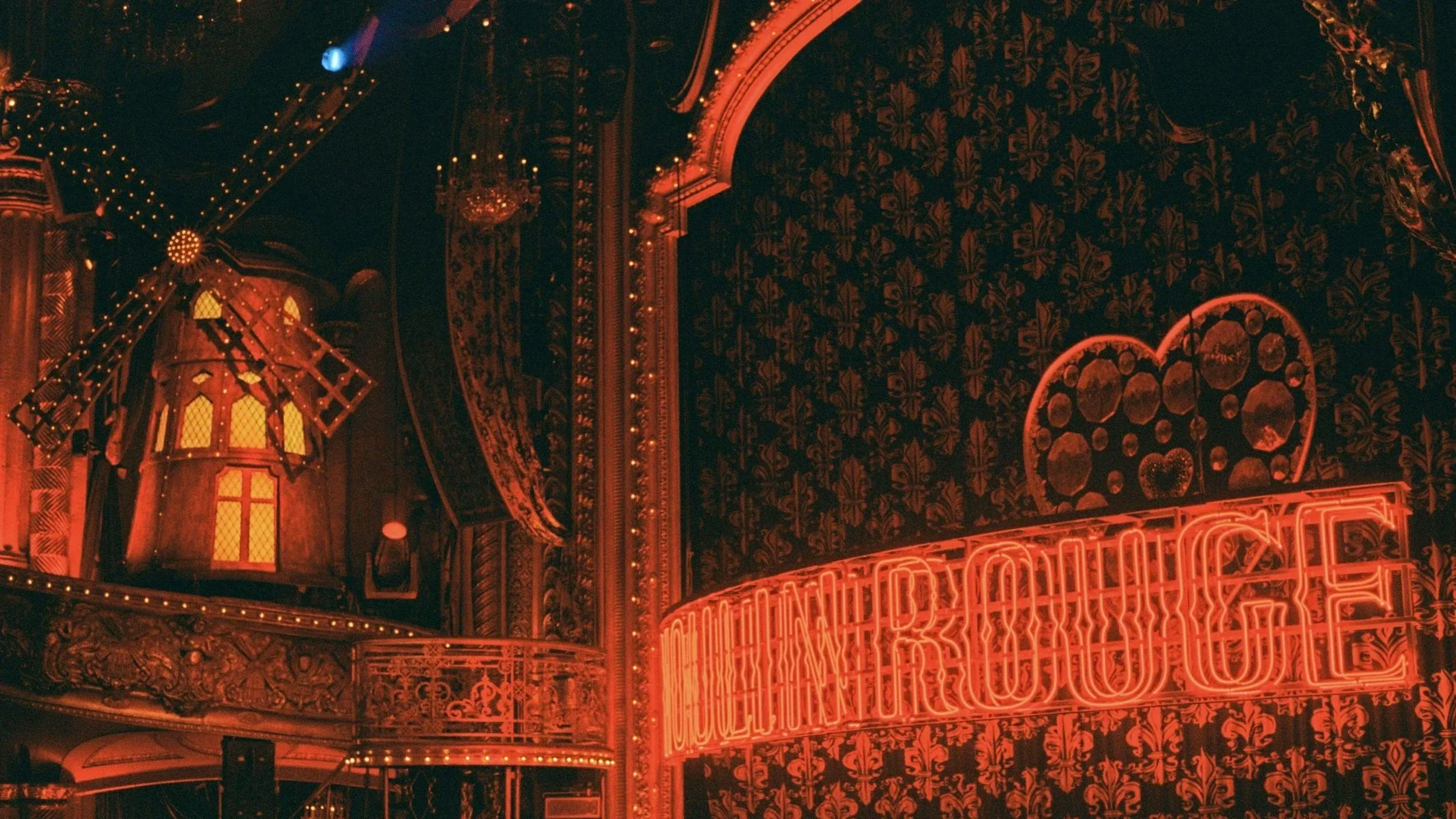 Interior of a theatre with ornate decor, a windmill decoration, string lights, and a bright neon sign that says "LOUNGING ROOM"
