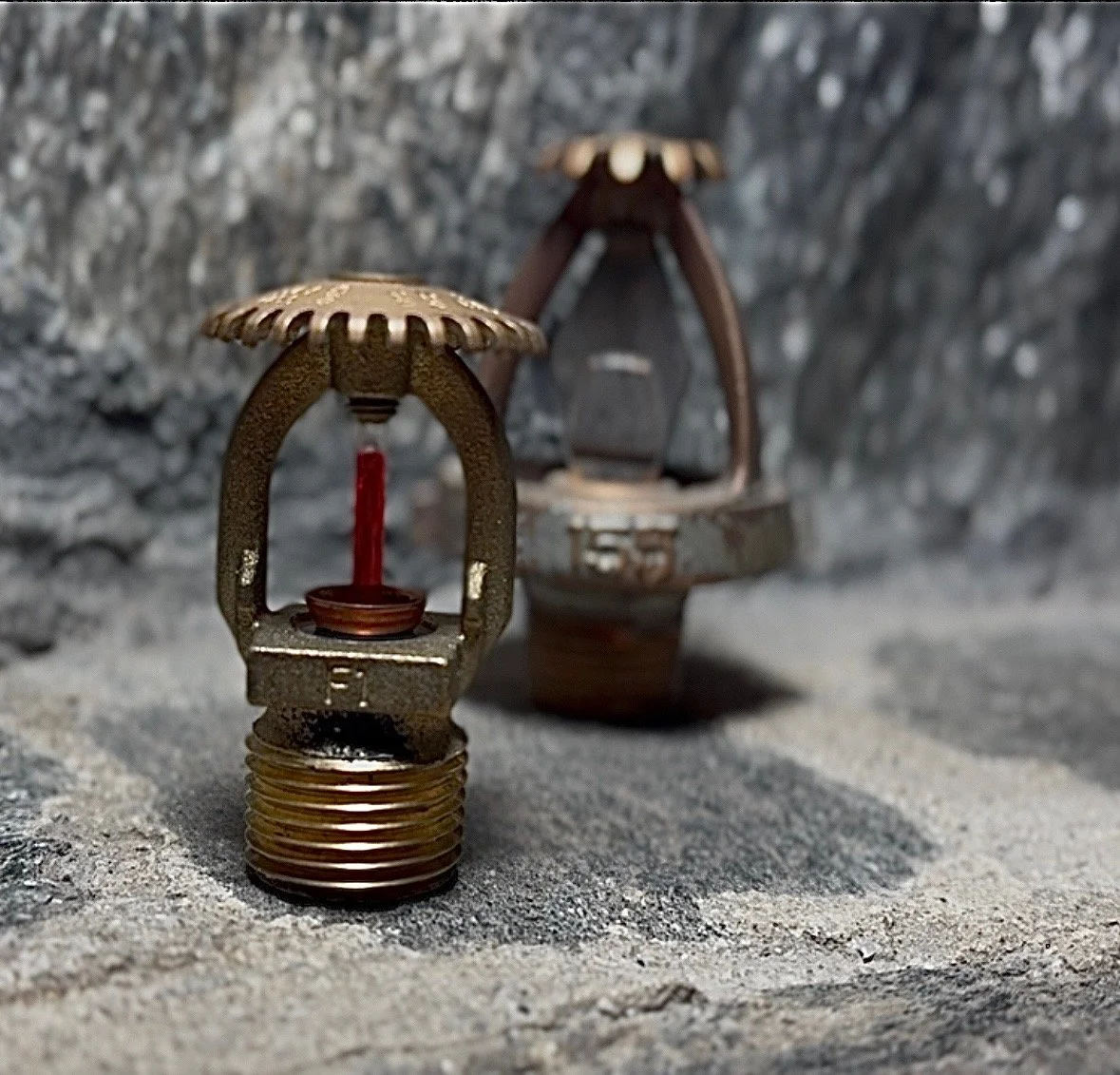 Close-up of two rusty, old lightbulb sockets with the sockets placed on sandy ground and a rocky background.
