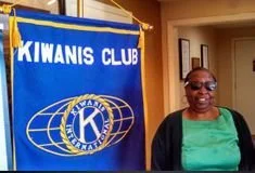 A woman standing next to a Kiwanis Club banner in a room.