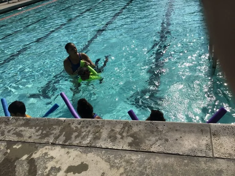 A swimming instructor teaching children how to swim in a pool.