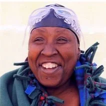 Close-up of smiling woman in medical protective gear, including a hair cover, in a healthcare setting.