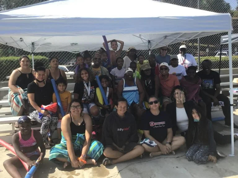 Group of diverse people posing under a white canopy at a sports field.