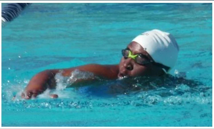 Swimmer practicing in a swimming pool wearing goggles, a swim cap, and a swimsuit