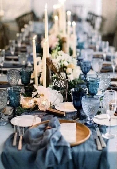 Elegant dining table setting with candles, flowers, blue glasses, and white plates.
