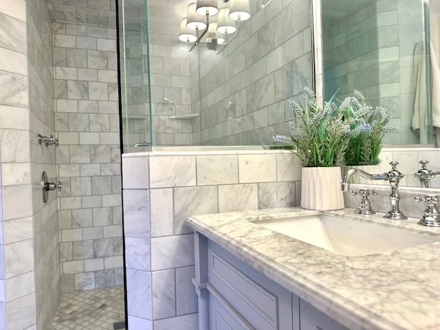 Close-up of white marble vanity with Newport Brass fixtures and fresh floral accents in a serene Metro Detroit master bathroom designed by NCIDQ-certified Sarah Gilpin for clients in Birmingham, Bloomfield Hills, and Grosse Pointe.