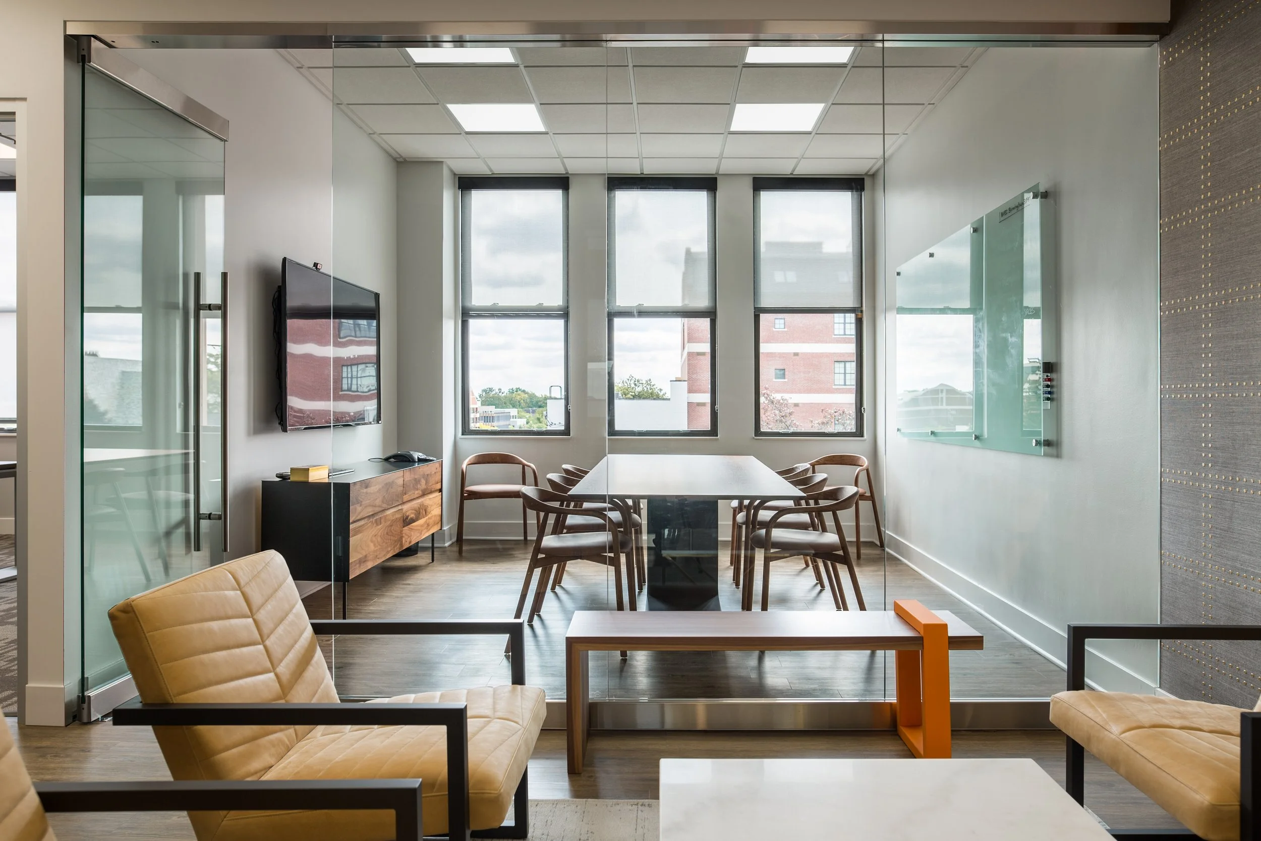 Modern commercial office conference room designed by Gilpin Design in Birmingham, Michigan – sleek glass-walled meeting space with warm leather seating and natural light for a private equity client.