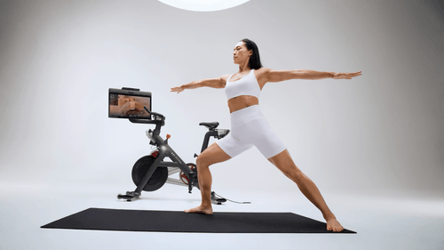 Woman practicing yoga in front of a stationary exercise bike in a studio