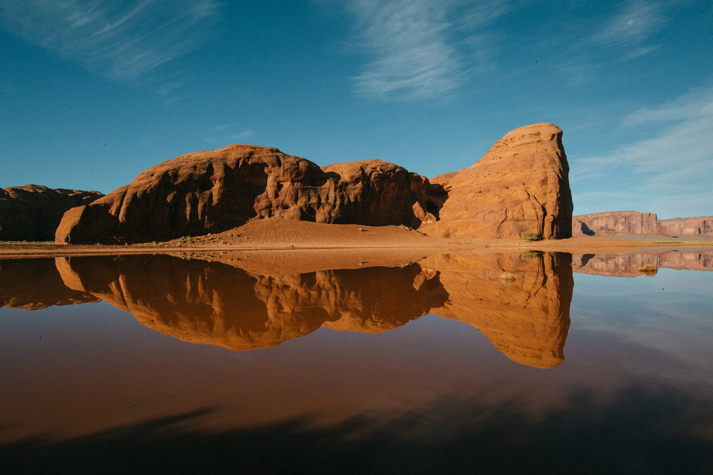 Rock formations reflected in a calm body of water with a clear blue sky.