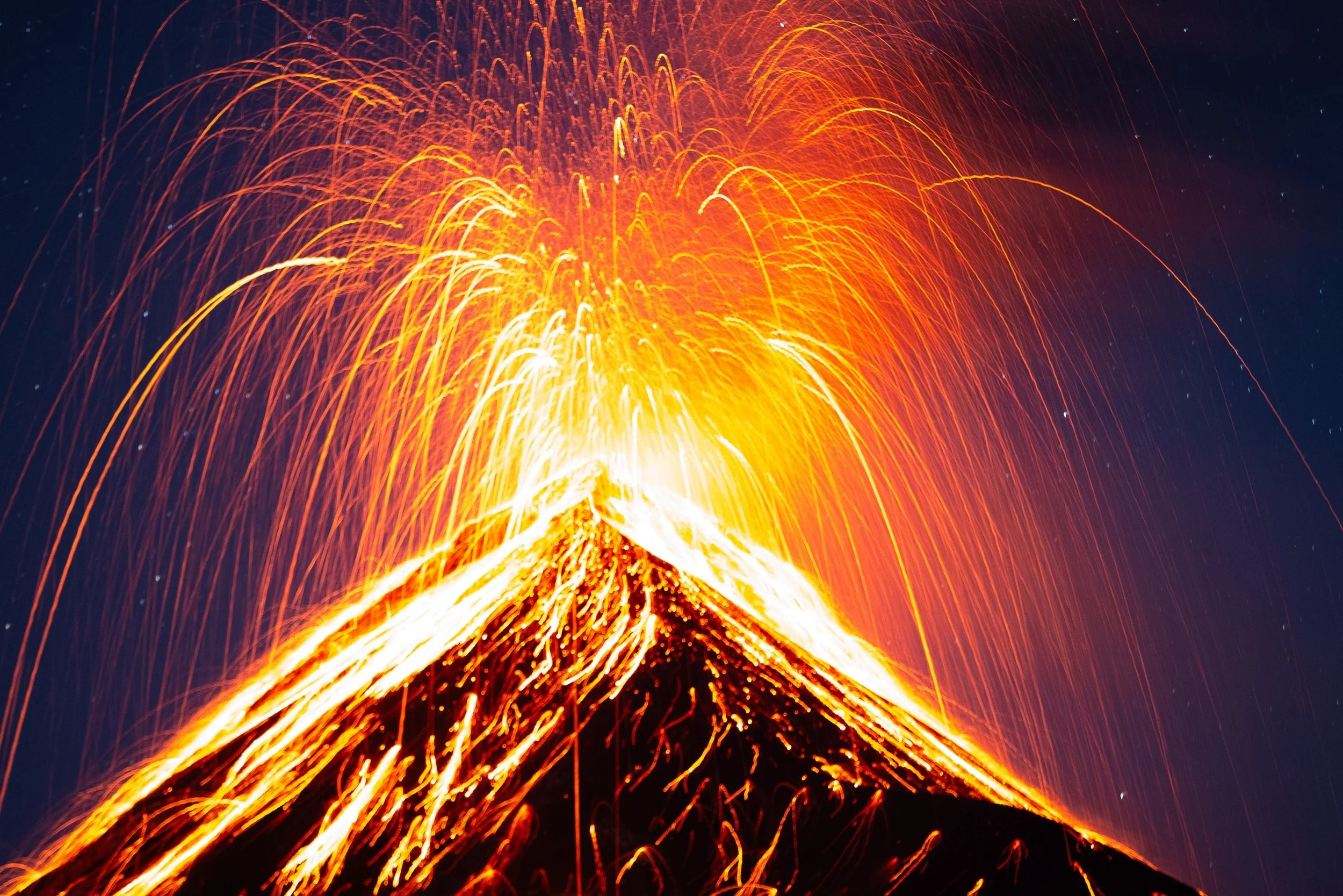 An erupting volcano spewing molten lava and bright orange sparks into the night sky.