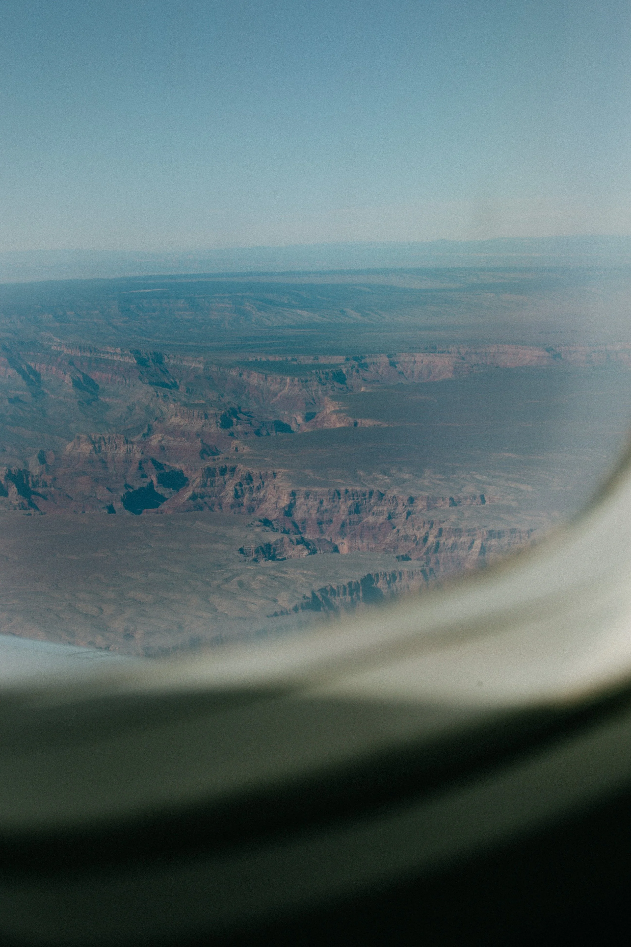 A view of the Grand Canyon from an airplane window, showing the canyon's layered rock formations and vast wilderness.
